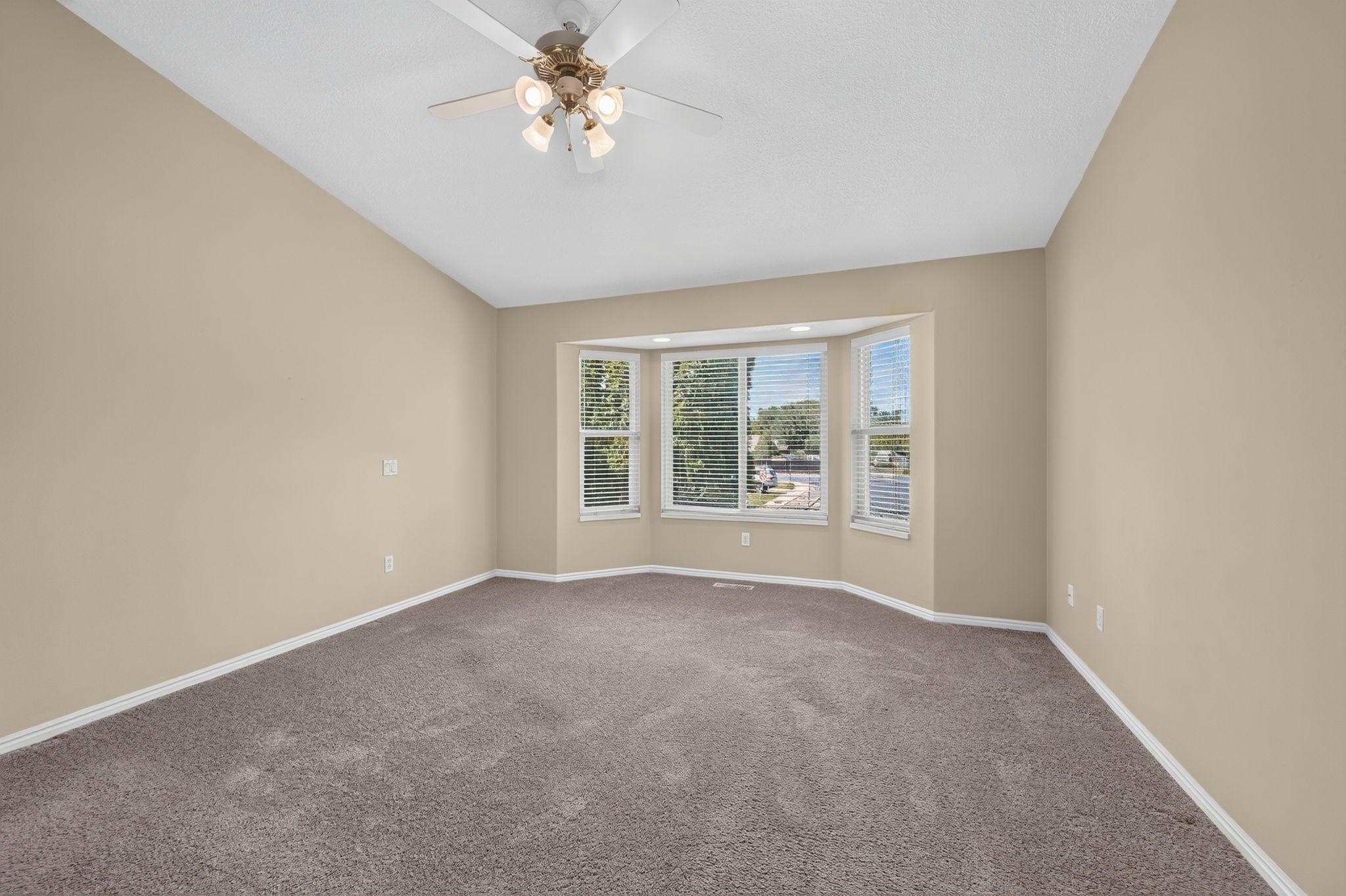 Bay window with horizontal blinds, sloped ceiling, overhead ceiling fan with integrated lighting, neutral-toned walls, and carpet flooring