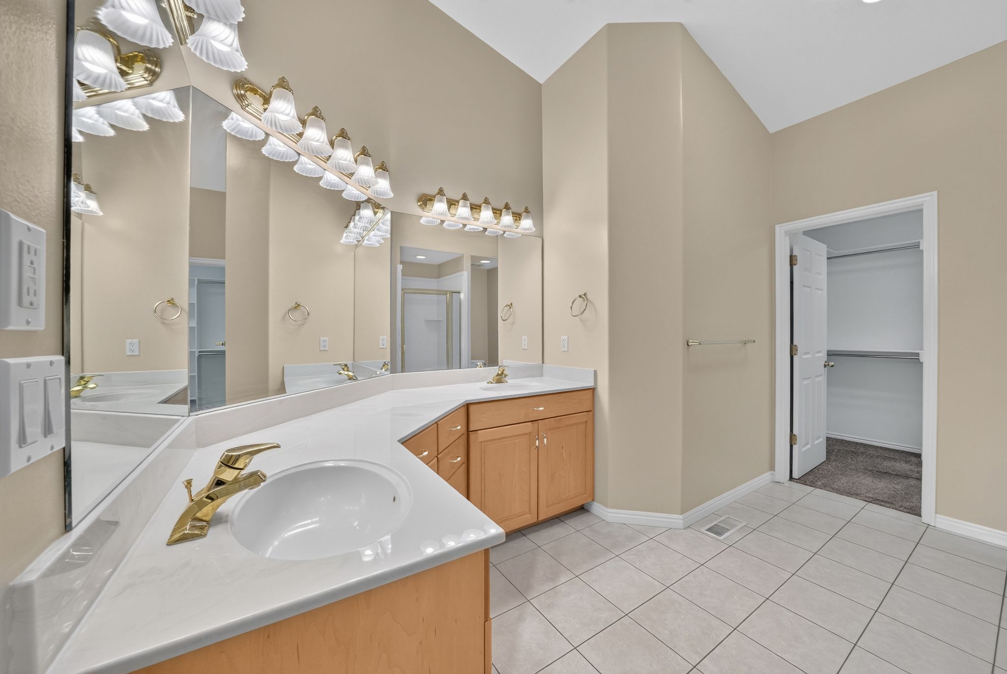 Bathroom featuring a dual vanity with light-tone wood cabinetry, white countertops, and gold-finish fixtures