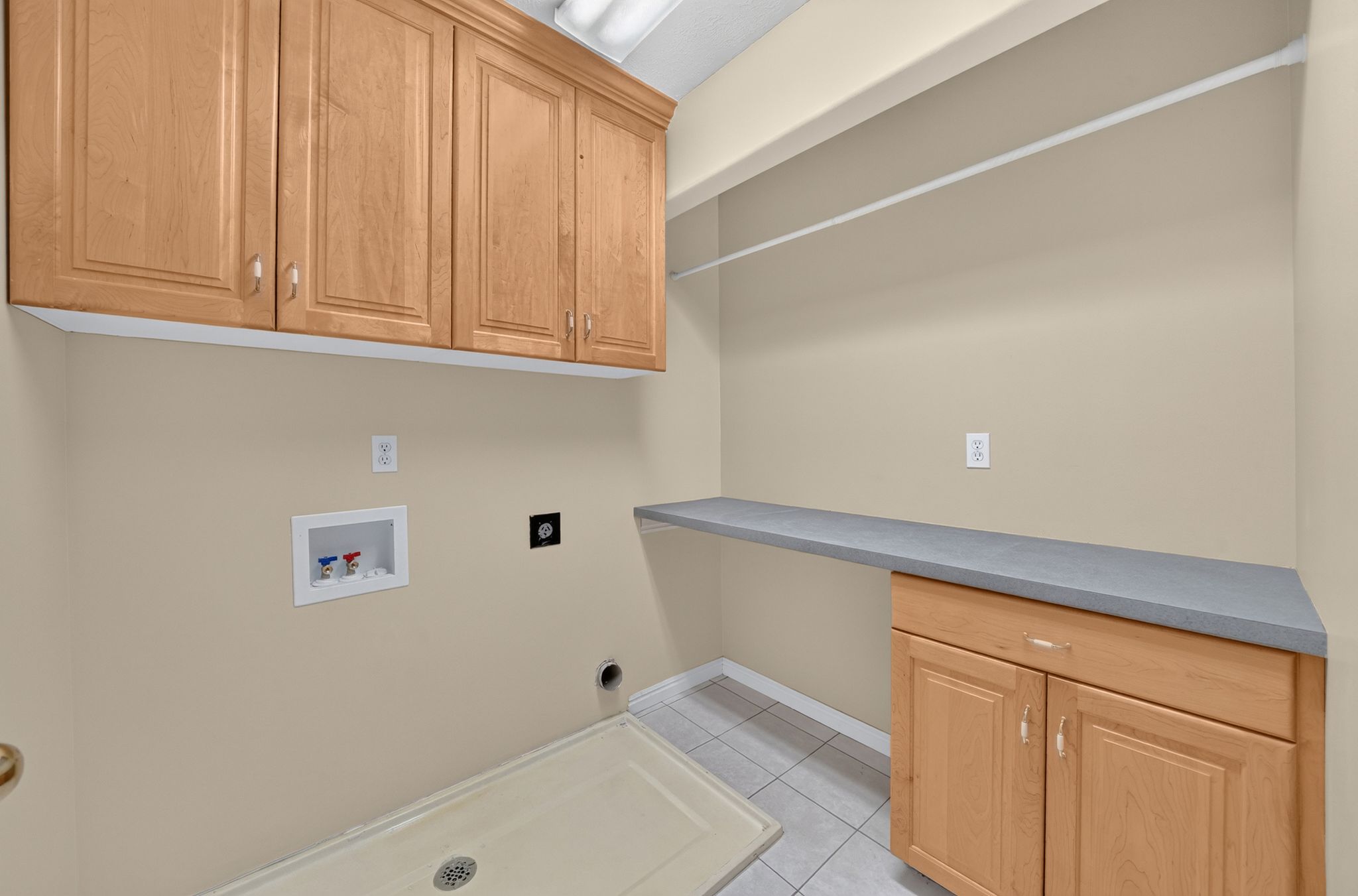 Laundry area featuring light wood cabinetry, a utility sink, a built-in countertop, and tile flooring