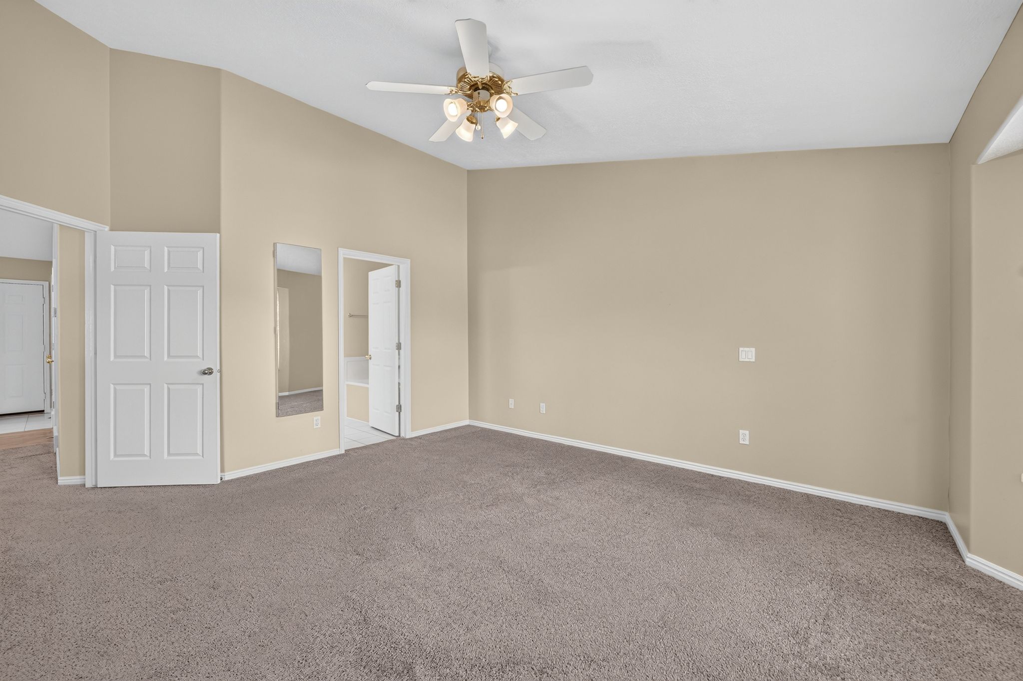 Spacious room featuring vaulted ceilings, a ceiling fan with integrated lighting, neutral-toned walls, and plush carpet flooring