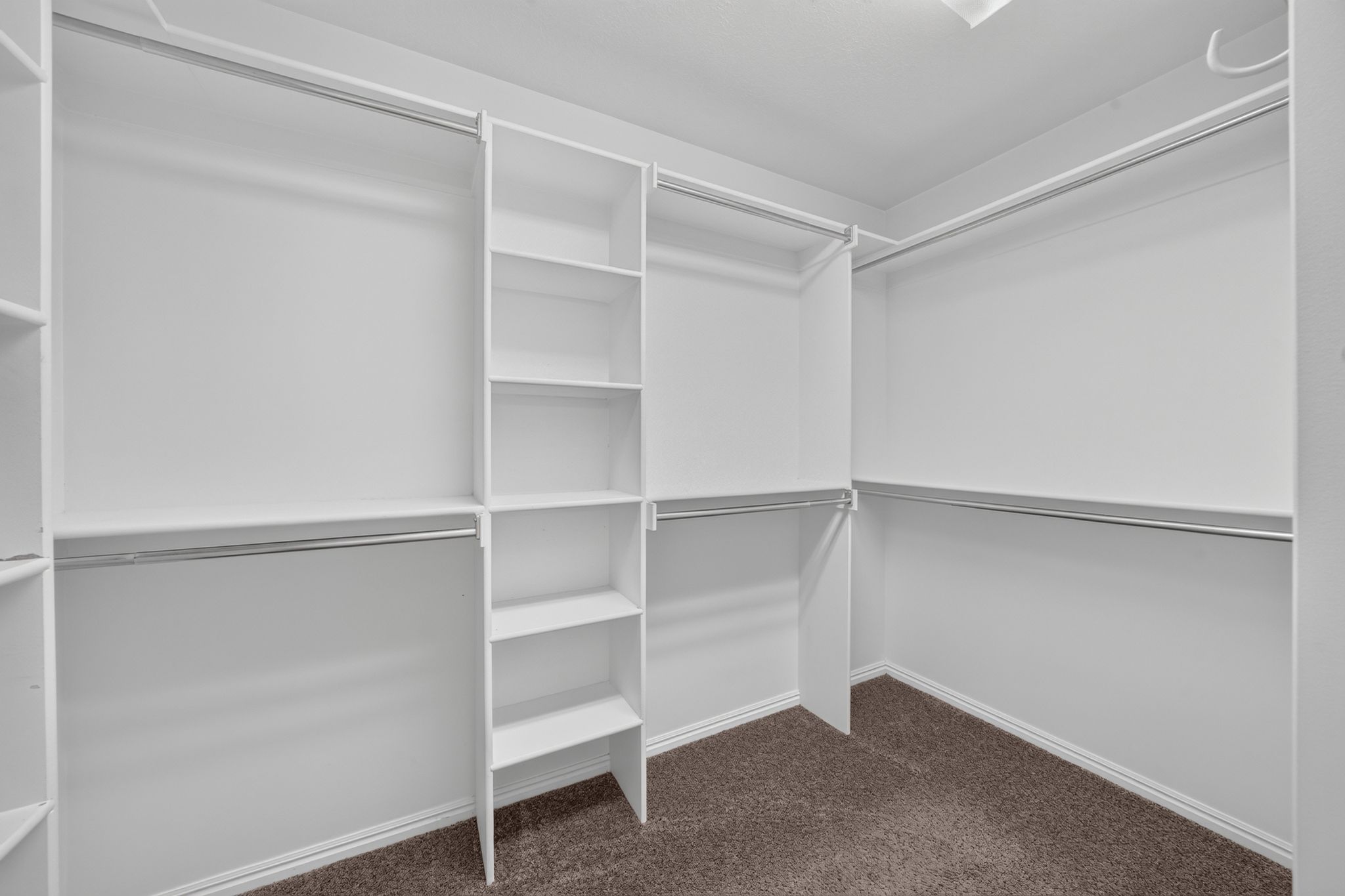 Walk-in closet featuring built-in white shelving, multiple hanging rods, and neutral-toned carpeting
