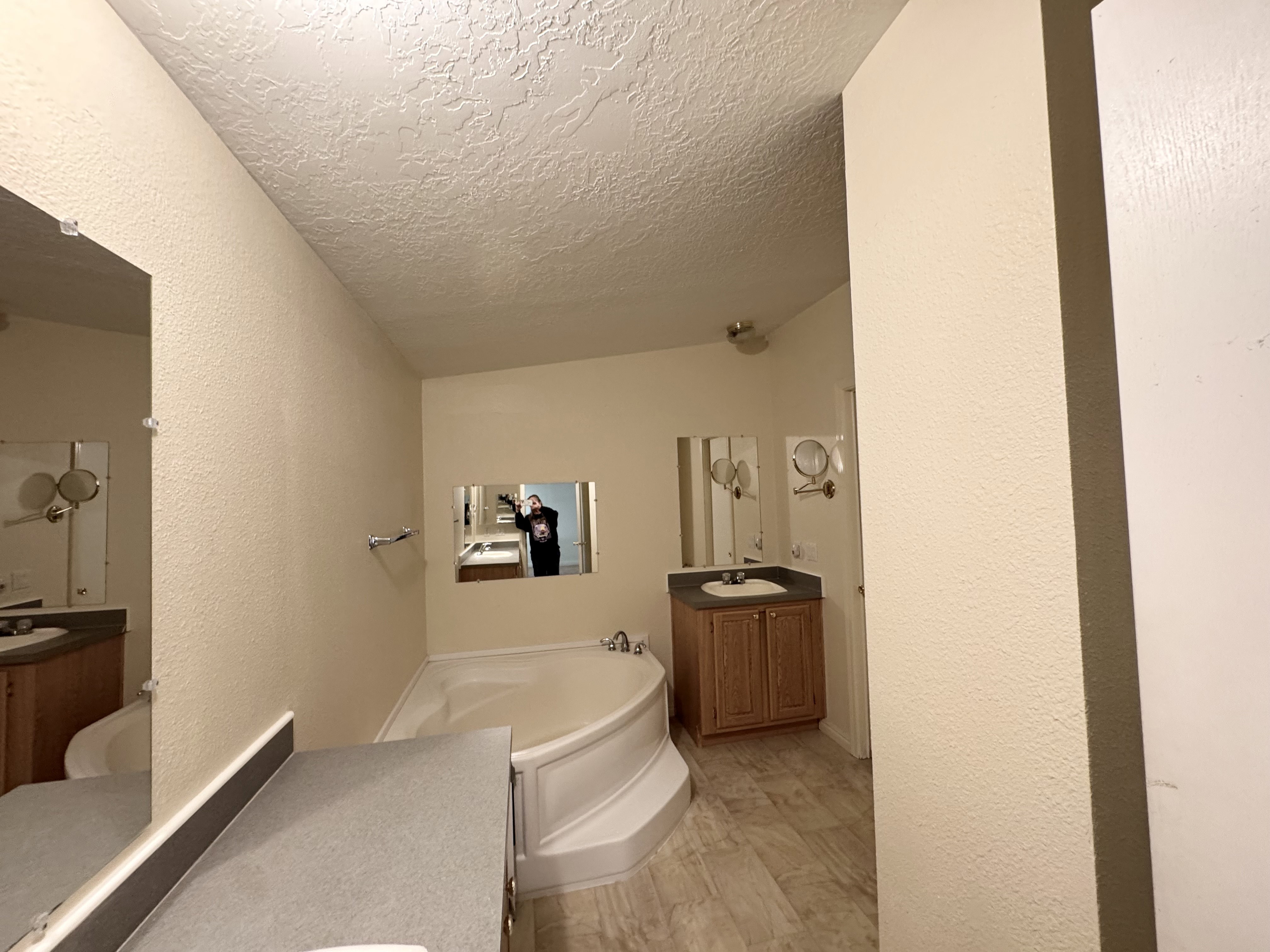 Bathroom featuring a built-in corner soaking tub, two separate vanity stations with single sinks, wood-finish cabinetry, and tiled flooring