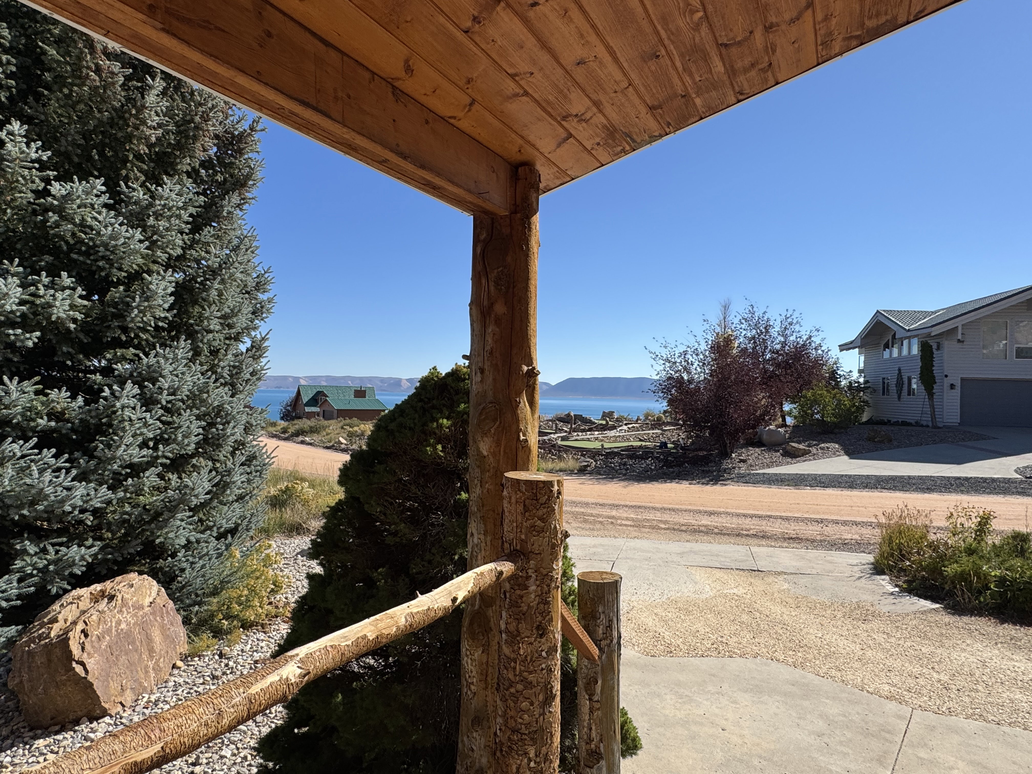 Covered porch featuring natural wood posts and railing, with a clear sky and distant water visible
