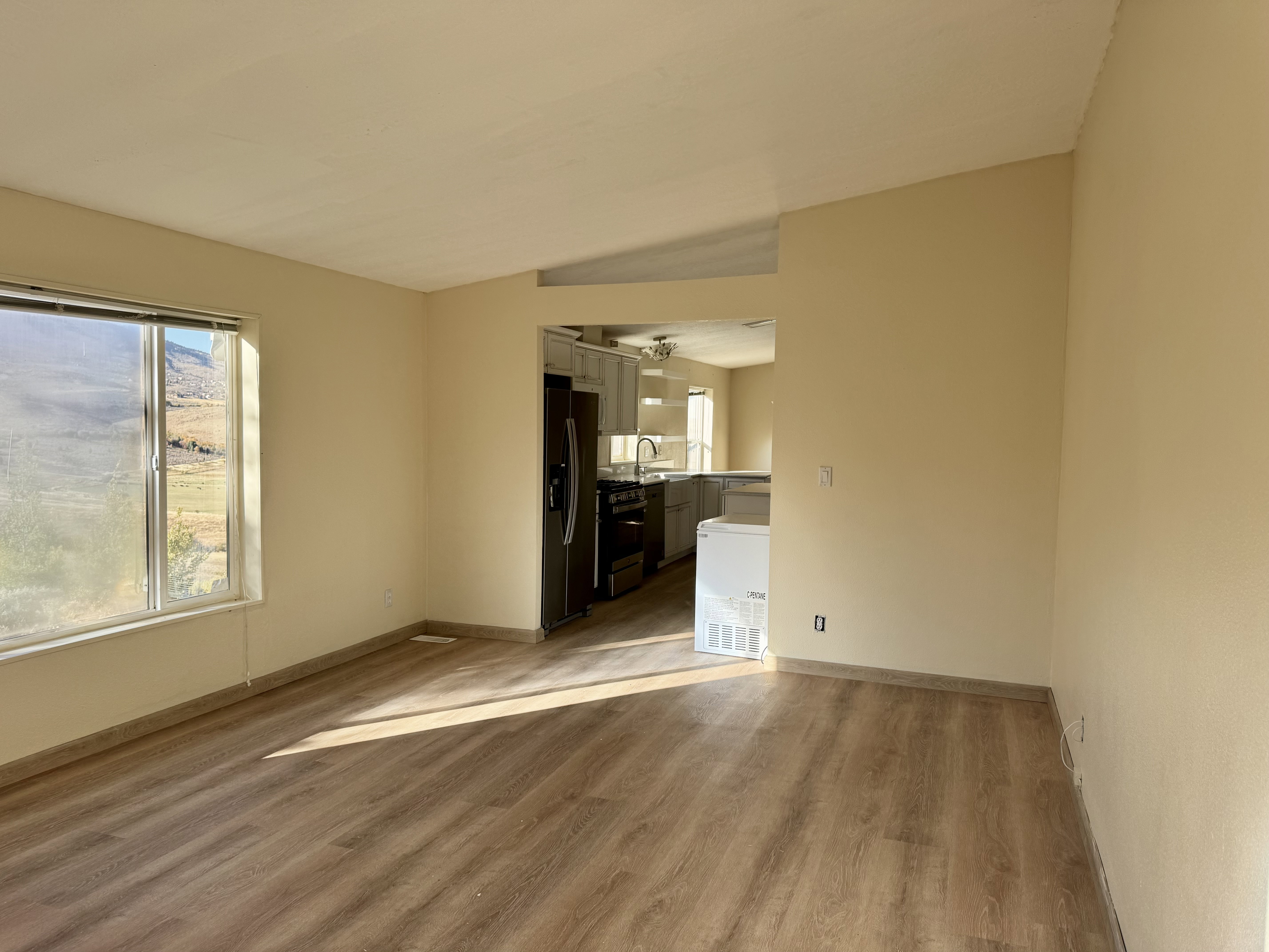 Open-concept living area featuring wood-finish flooring and a large window overlooking natural scenery