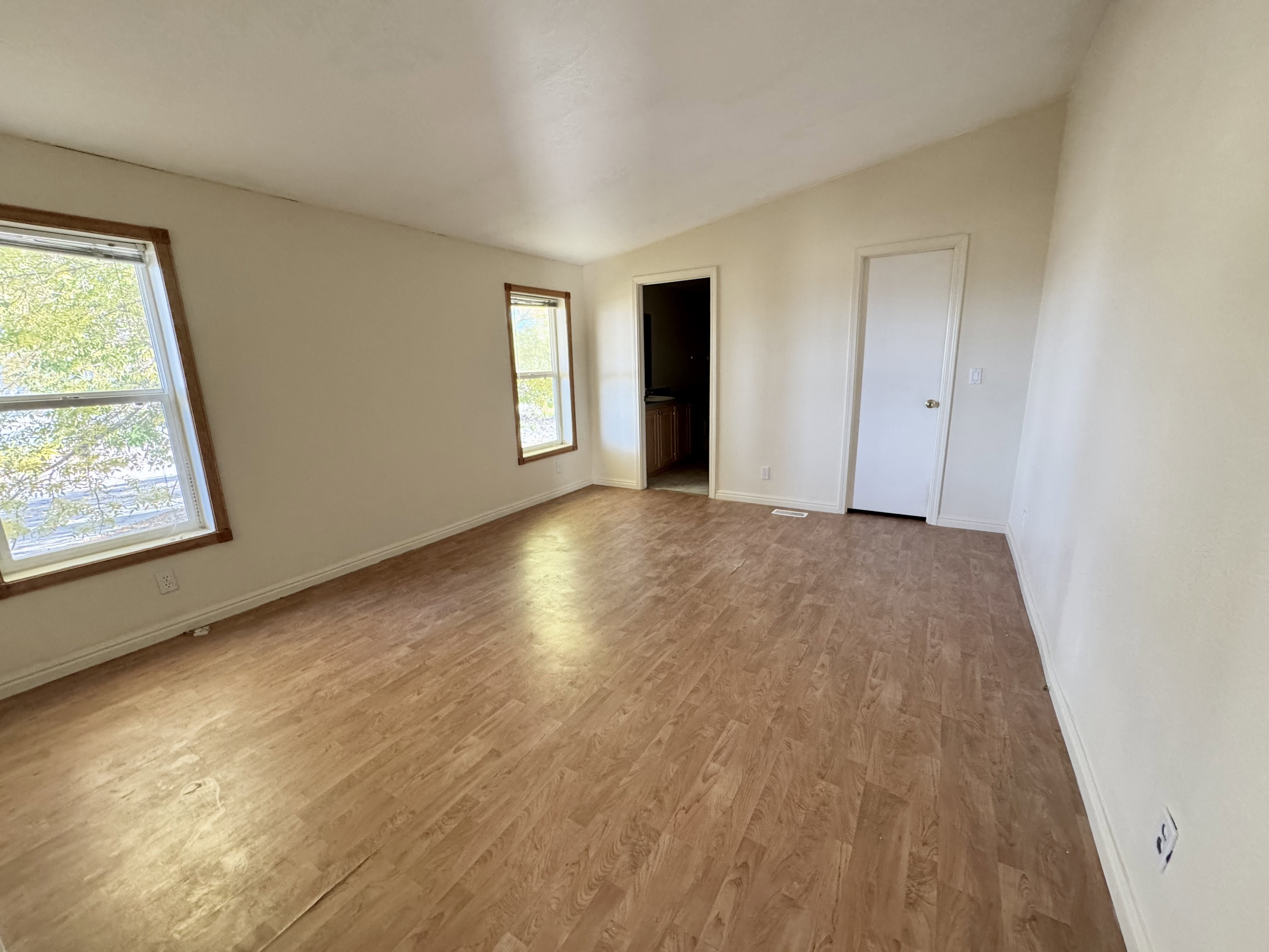Spacious room featuring wood-finish flooring, two windows with wood trim, and a high vaulted ceiling