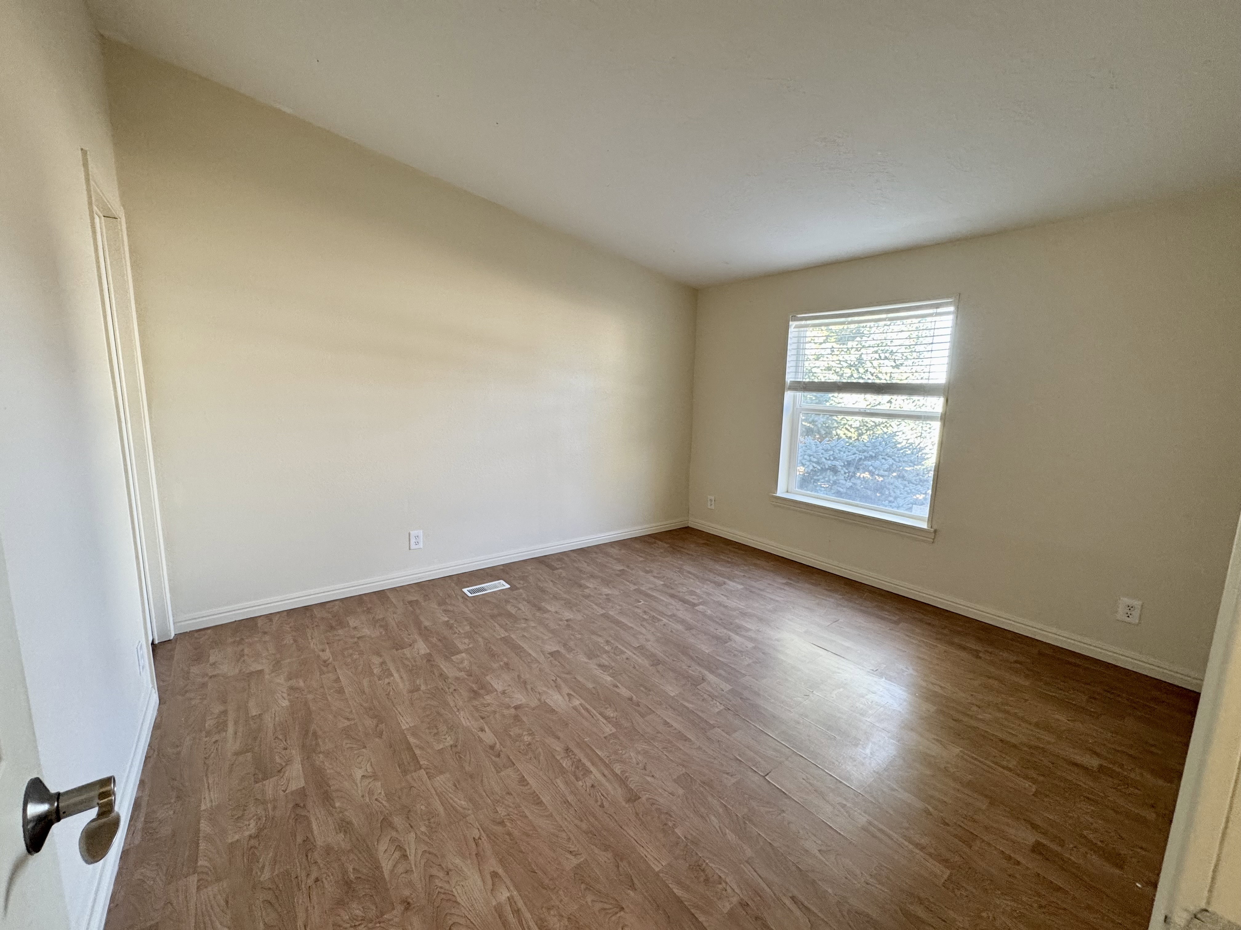 Spacious room featuring wood-finish flooring, a single window with blinds, and neutral-toned walls