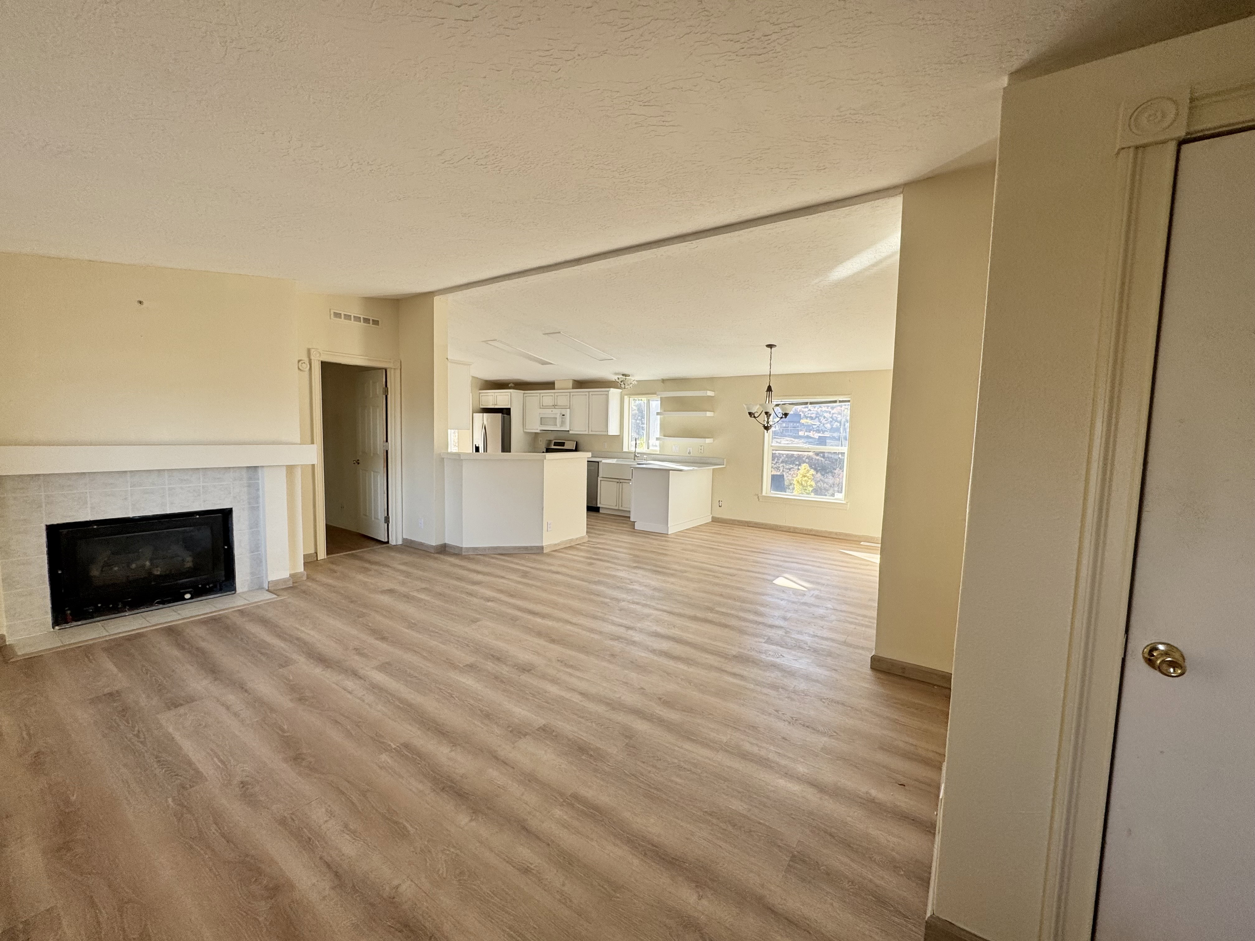 Open-concept living area featuring wood-finish flooring throughout, a tiled fireplace with a white mantel, and a kitchen with white cabinetry and a built-in breakfast bar