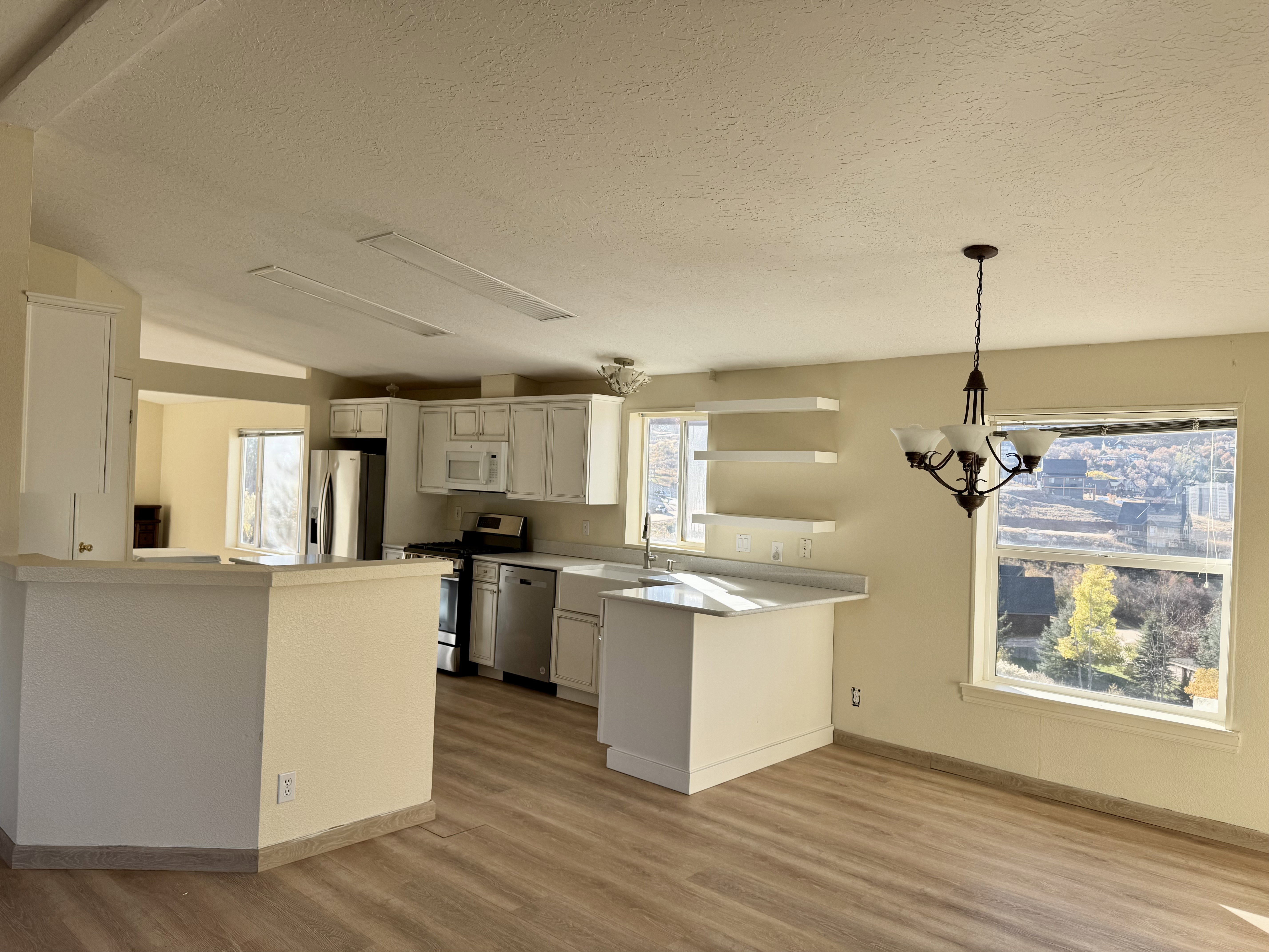 Open-concept kitchen and dining area featuring light wood-finish flooring, white cabinetry, stainless steel appliances, and a central island with a breakfast bar