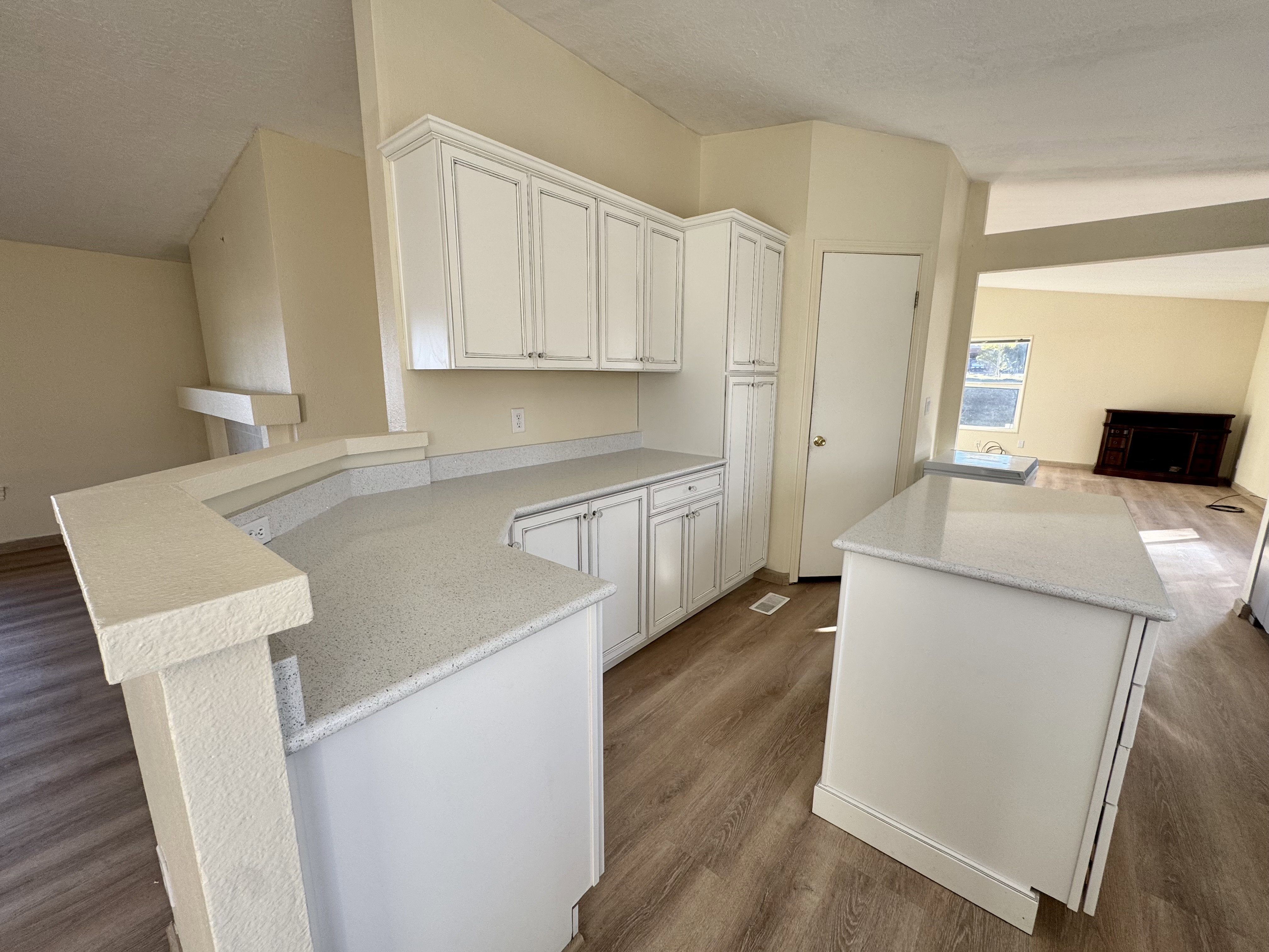 Kitchen featuring white cabinetry, light-toned countertops, a multi-level breakfast bar, a central island, and wood-finish flooring