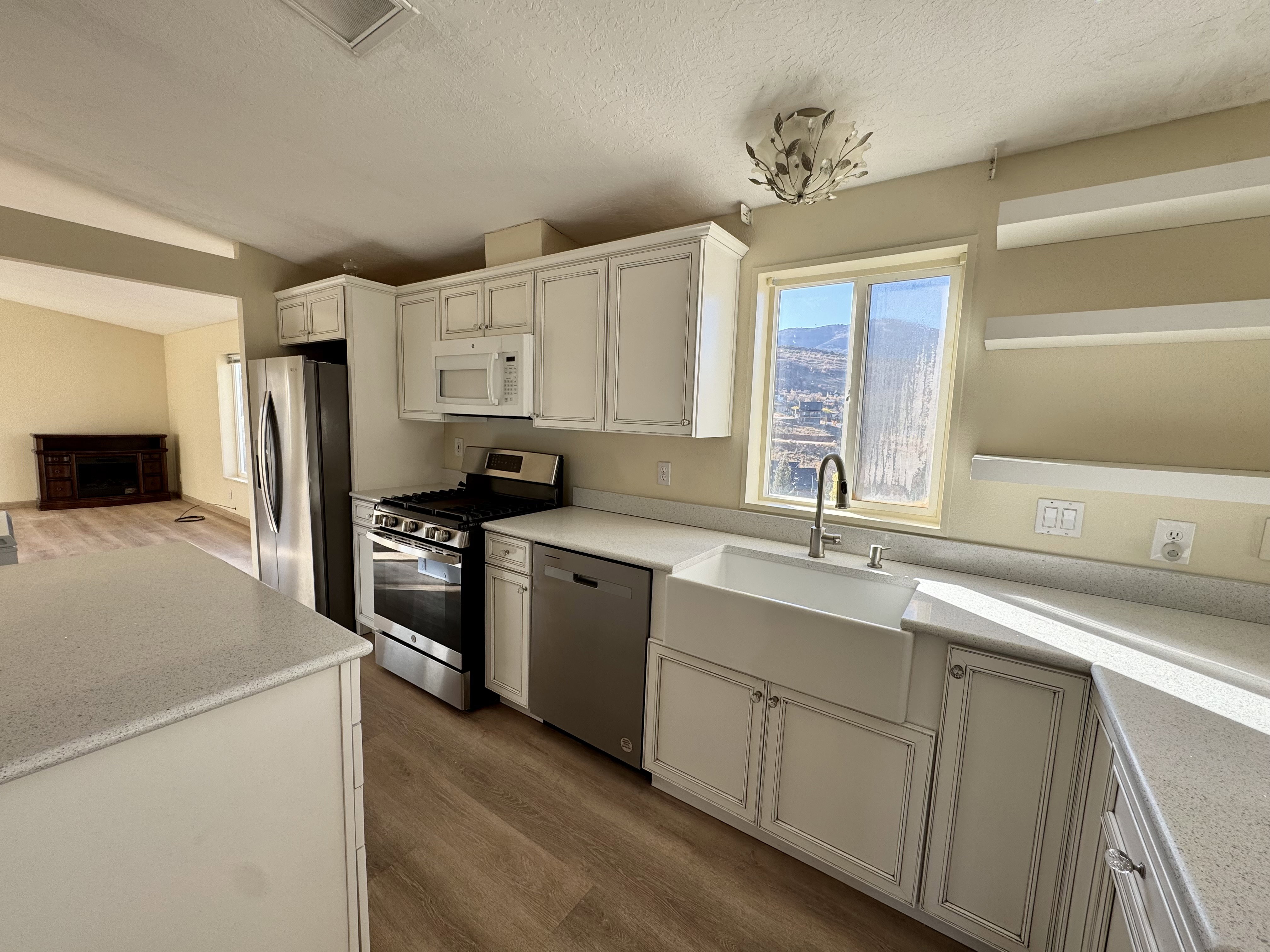 Kitchen featuring white shaker-style cabinetry, light speckled countertops, a large farmhouse sink, stainless steel appliances, and wood-finish flooring