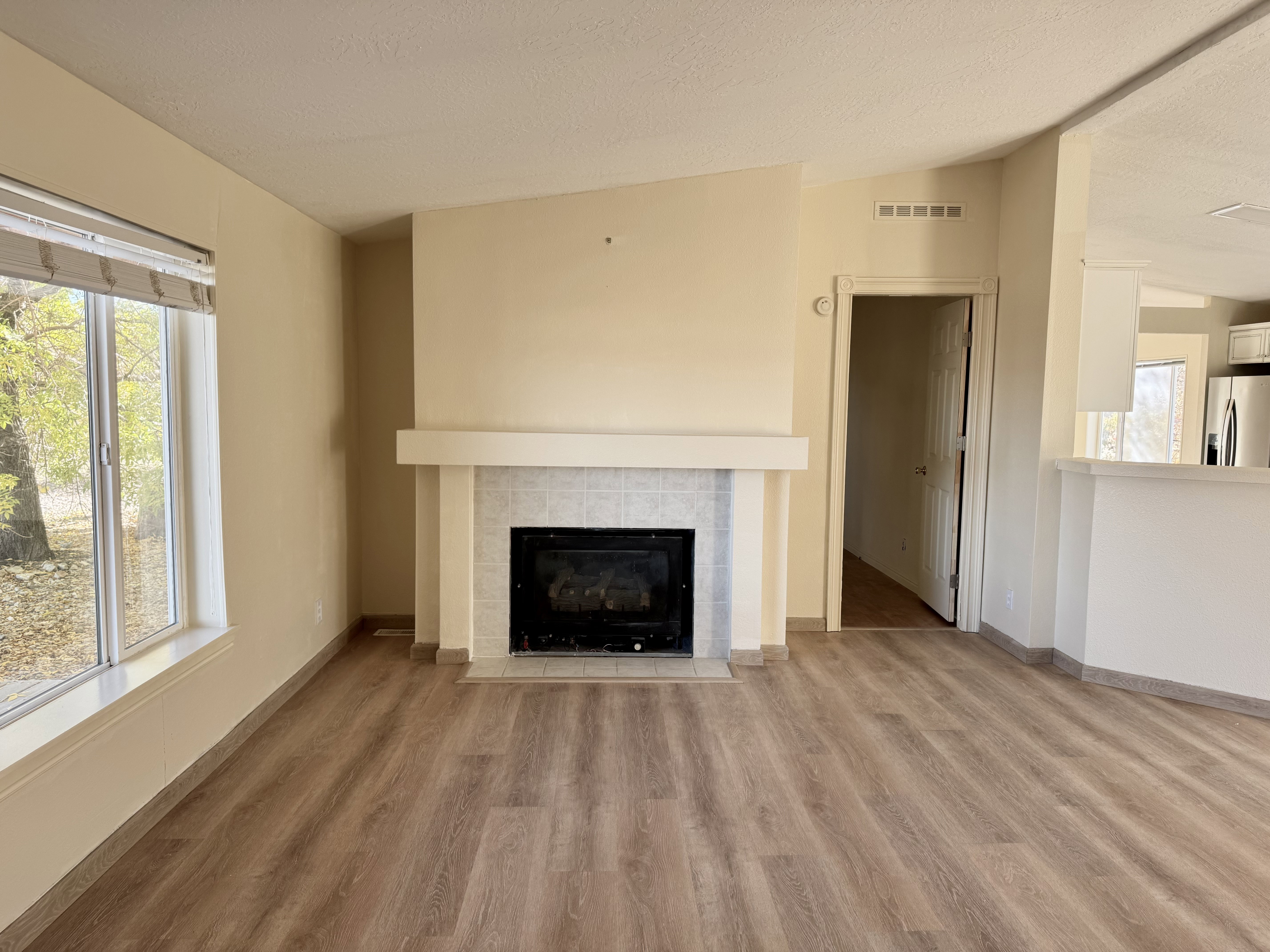 Living area featuring a fireplace with a tiled surround and mantel, wood-finish flooring, and a large window
