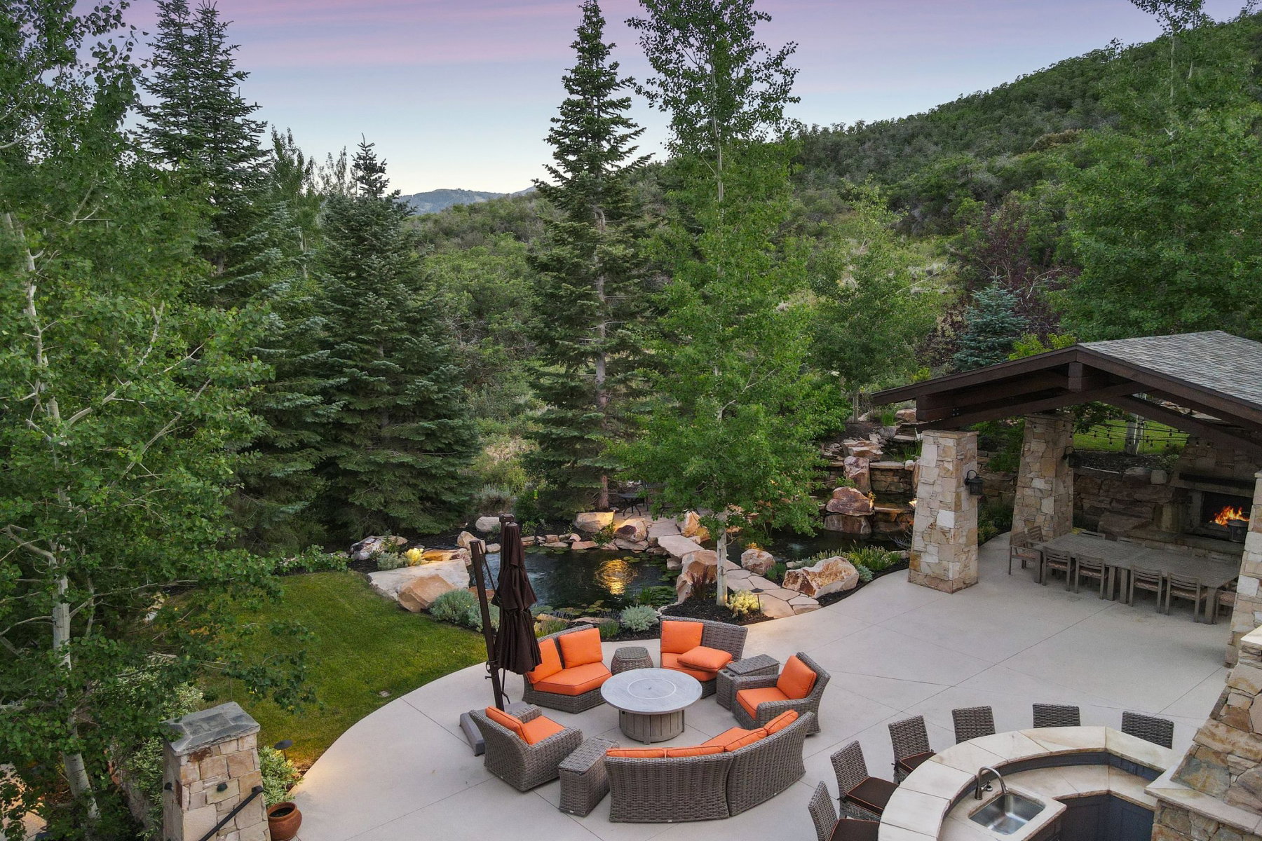 Expansive outdoor living area featuring a stone fireplace, integrated outdoor kitchen with sink, and a multi-level water feature
