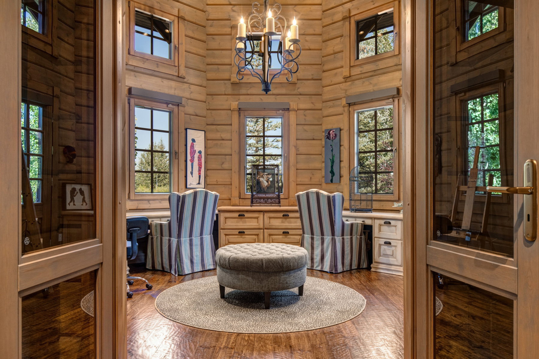 Paneled double doors open to a round room featuring extensive natural wood paneling, multiple windows, built-in cabinetry, and a wrought iron chandelier
