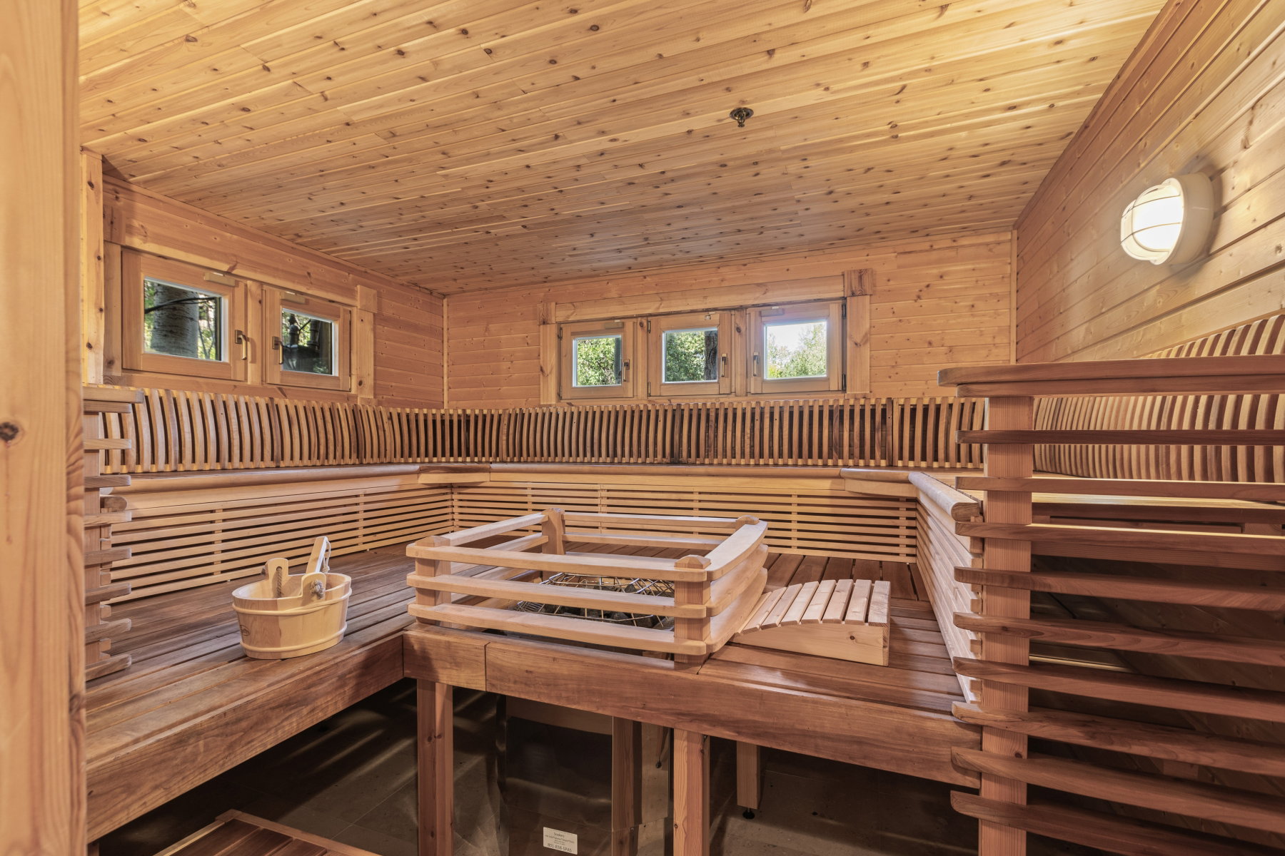 Dedicated sauna room featuring natural wood paneling throughout, multi-tiered bench seating, and a built-in heater with protective railing