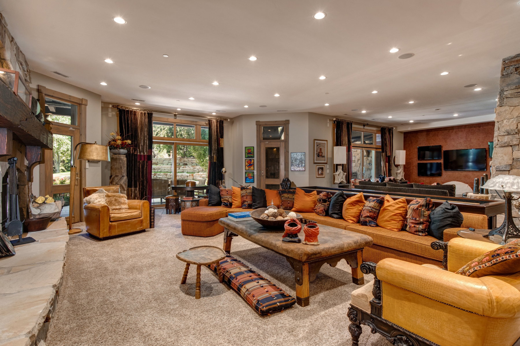 Spacious living area featuring a prominent stone fireplace, large windows, recessed lighting, wood-finish window frames, and soft carpet flooring