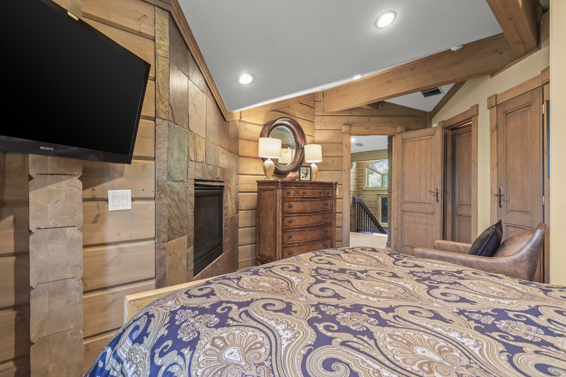 Stone accent wall with built-in fireplace, wood-planked walls, and exposed wood beams