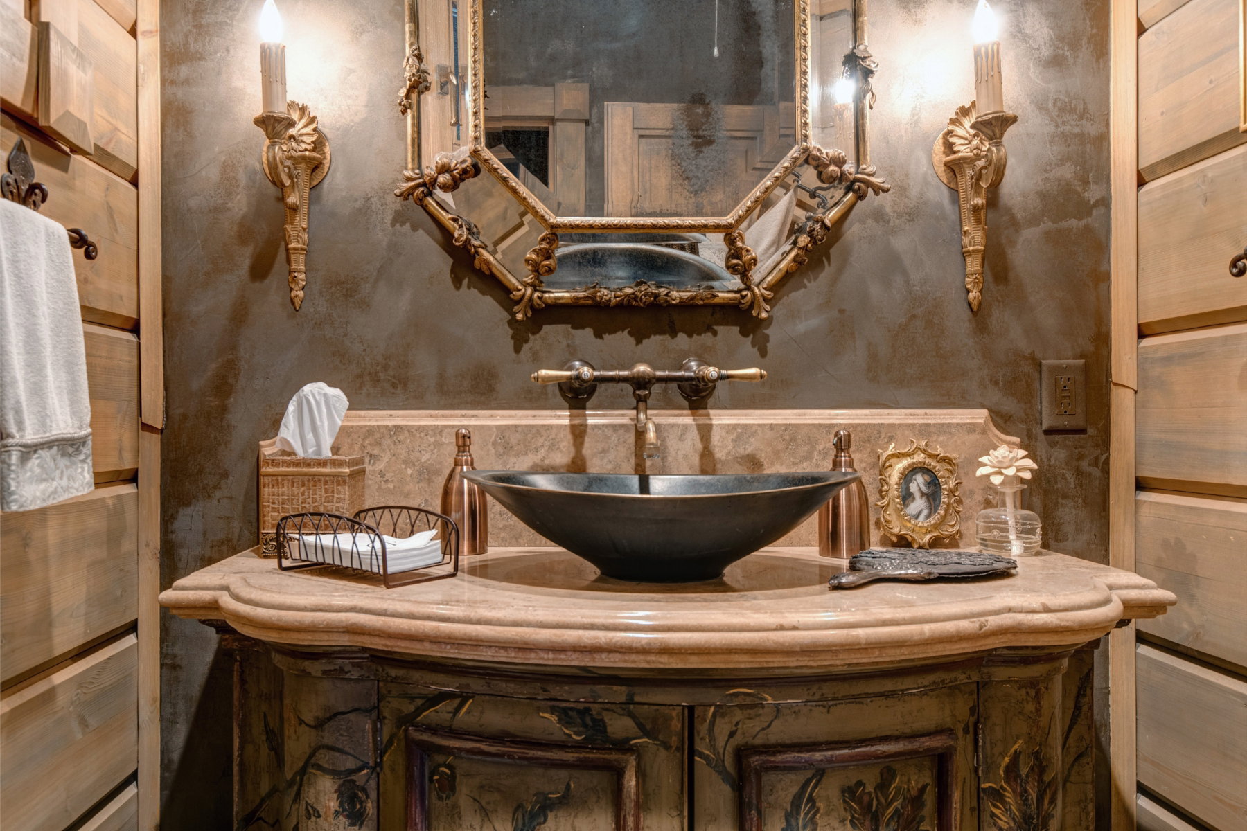 Custom vanity with a rounded stone countertop, black vessel sink, and an ornate gold-framed mirror