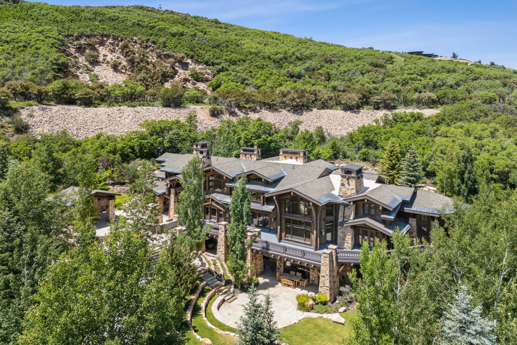 Expansive residence featuring a stone and wood facade, multiple balconies, a terraced lawn, and mature trees