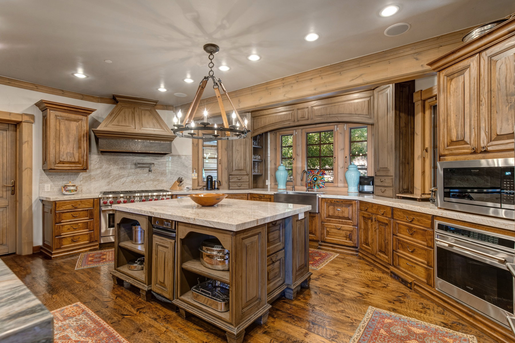 Gourmet kitchen featuring a large central island with light-toned countertop, extensive wood cabinetry, and wood-finish flooring