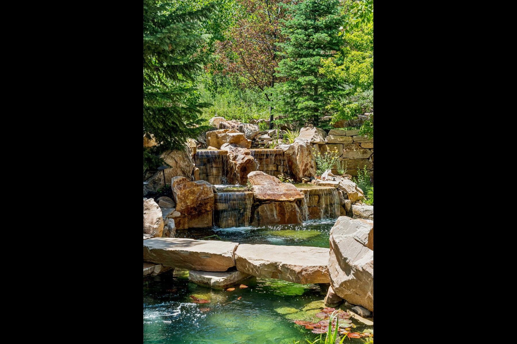 Multi-tiered rock waterfall feature with a natural stone bridge spanning a tranquil pond