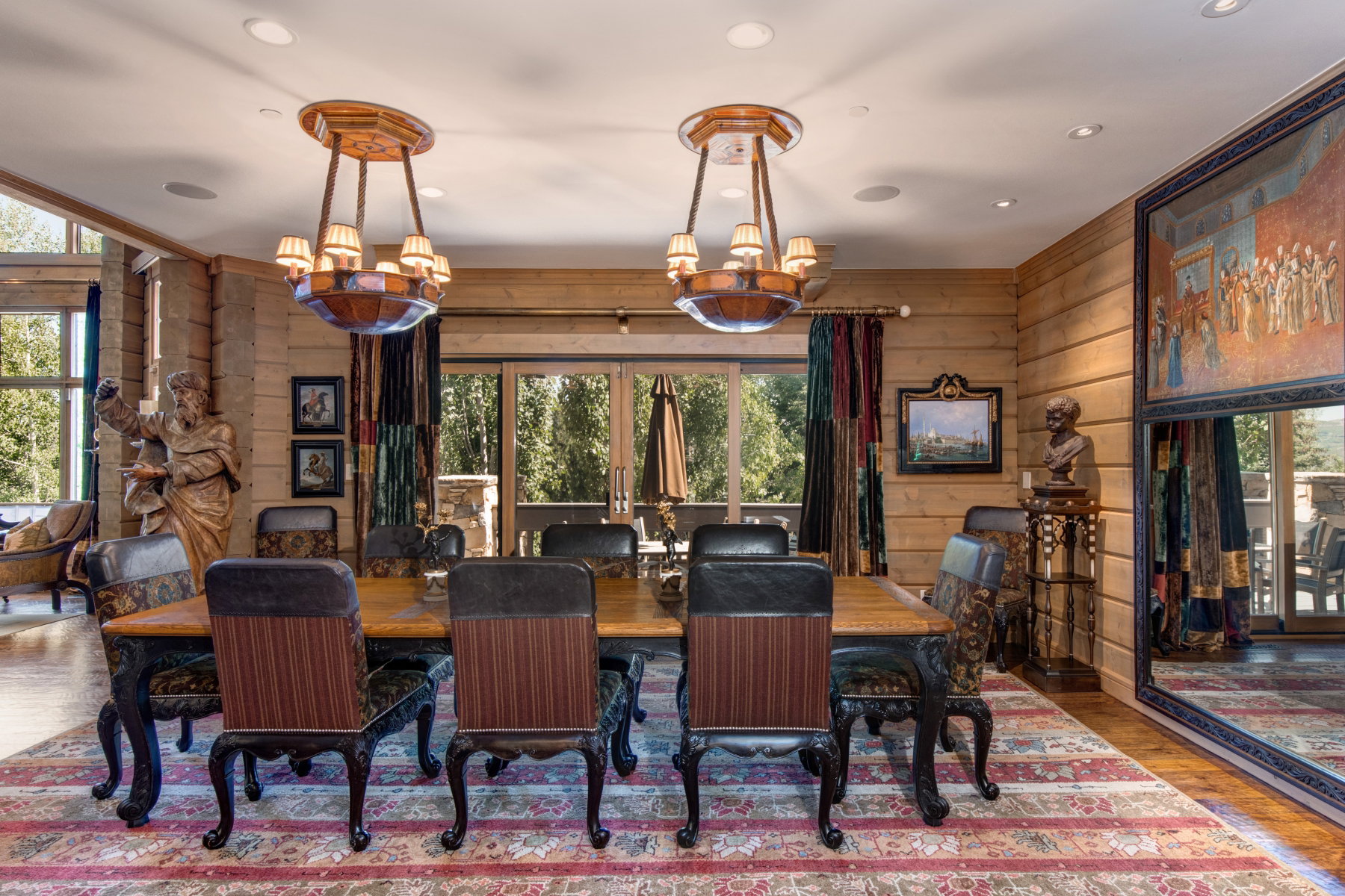 Dining area featuring wood plank walls, two ornate chandeliers, and a large dining table with six chairs