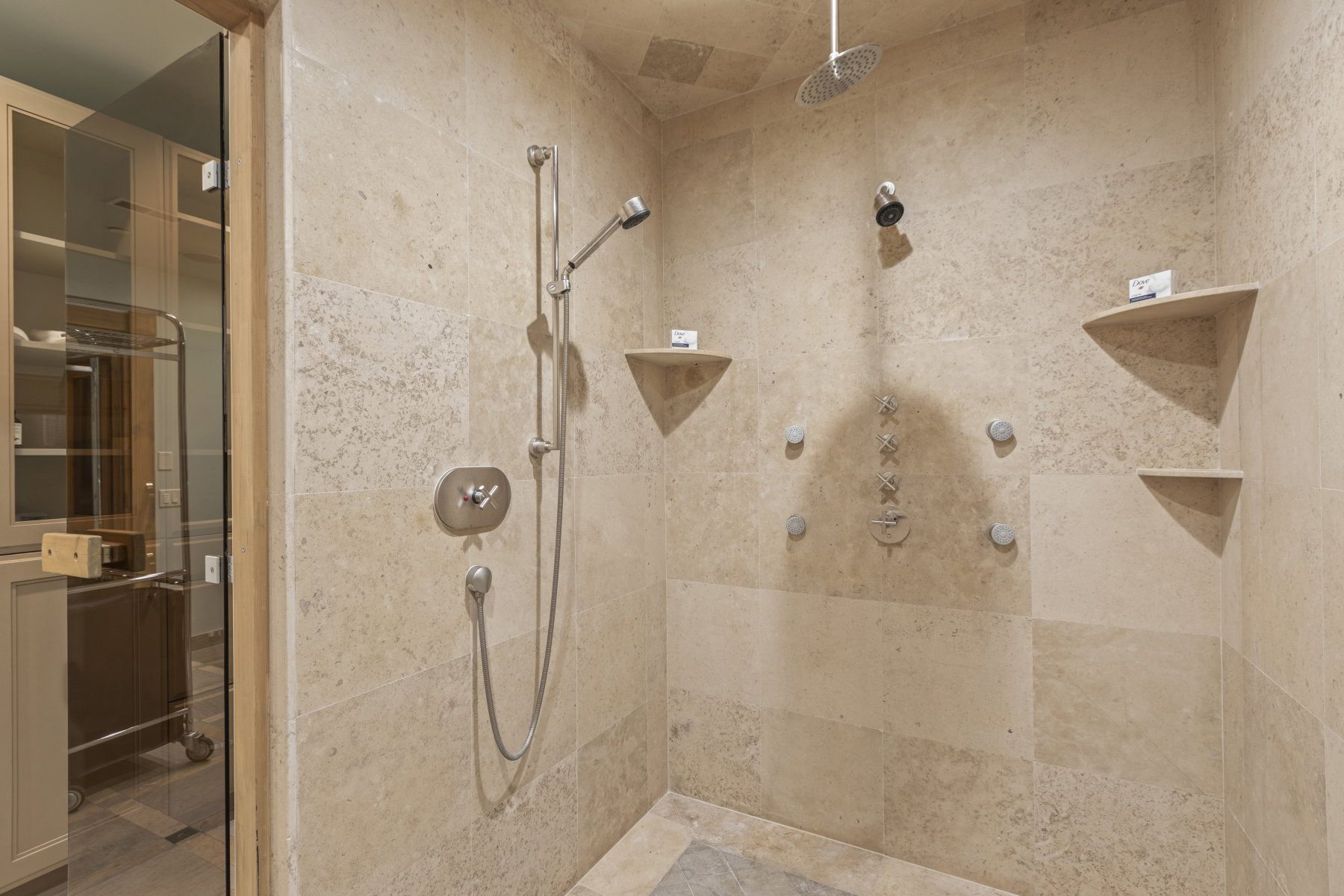 Stone-tiled shower featuring a ceiling-mounted rainfall showerhead, handheld shower fixture, and multiple body jets