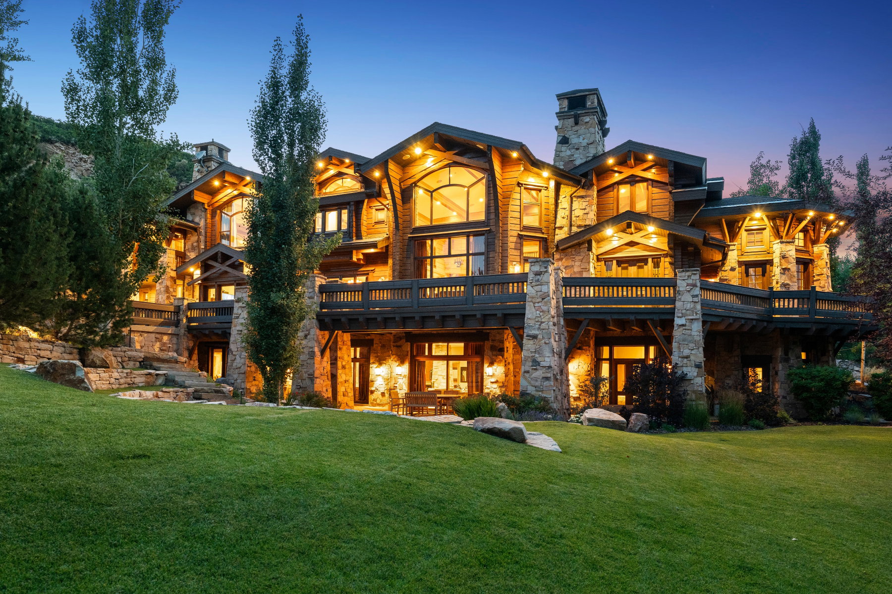 Stone and wood-clad multi-story residence featuring extensive balconies, a stone chimney, and large windows