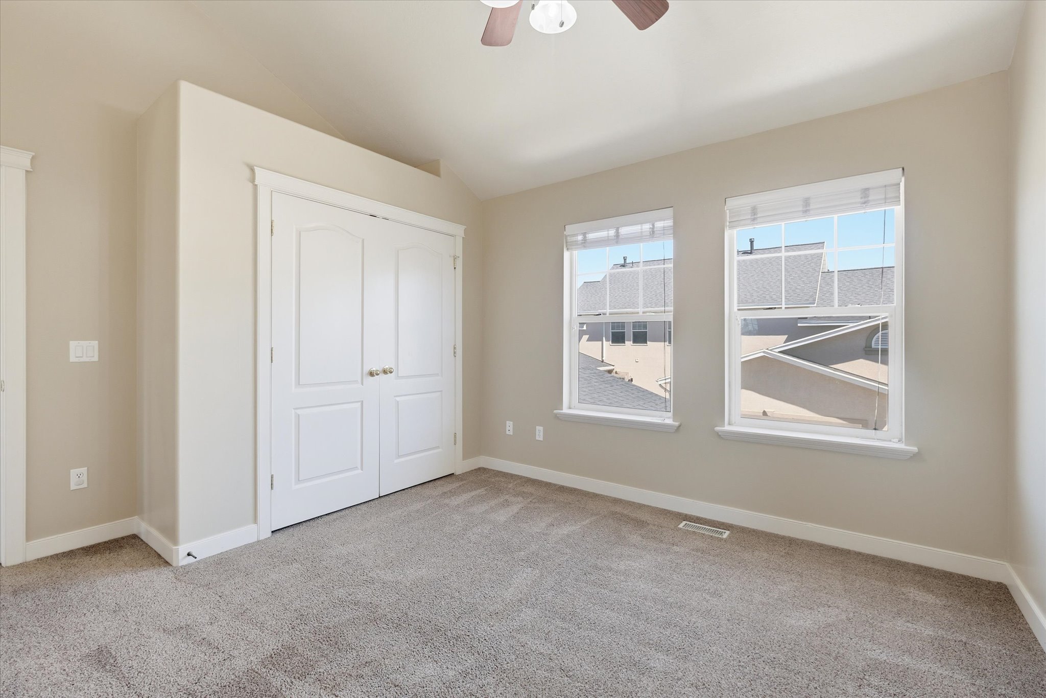 Carpeted room featuring dual windows with blinds, a double-door closet, a ceiling fan with integrated lighting, and neutral wall tones