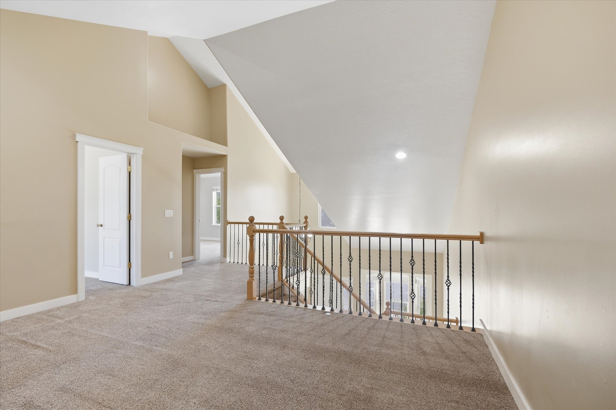Upper-level landing featuring vaulted ceilings, neutral-toned carpeting, and a decorative wrought iron and wood baluster railing