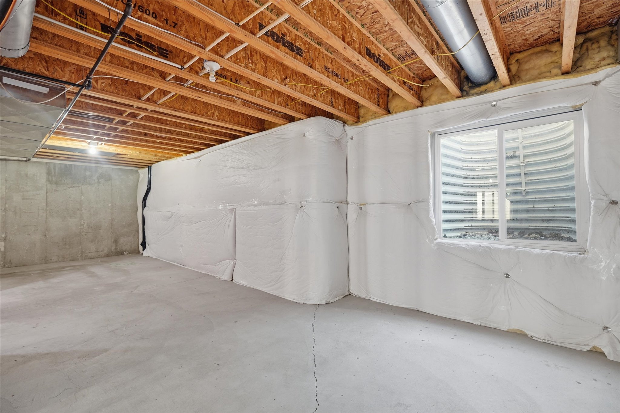 Unfinished basement space featuring exposed wood joists and concrete flooring