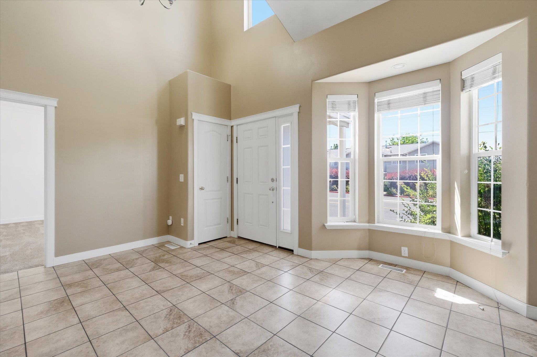 Foyer featuring a high vaulted ceiling, large bay windows, neutral-toned tile flooring, and a double entry door