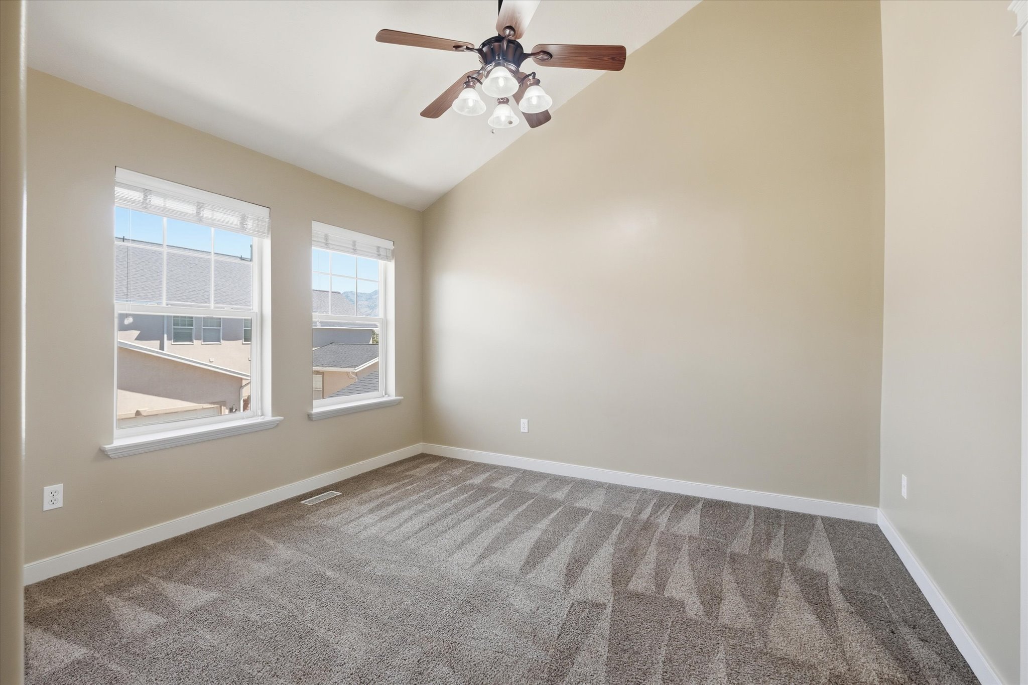 Room with vaulted ceiling, two large windows, textured carpet, and a ceiling fan with light fixture