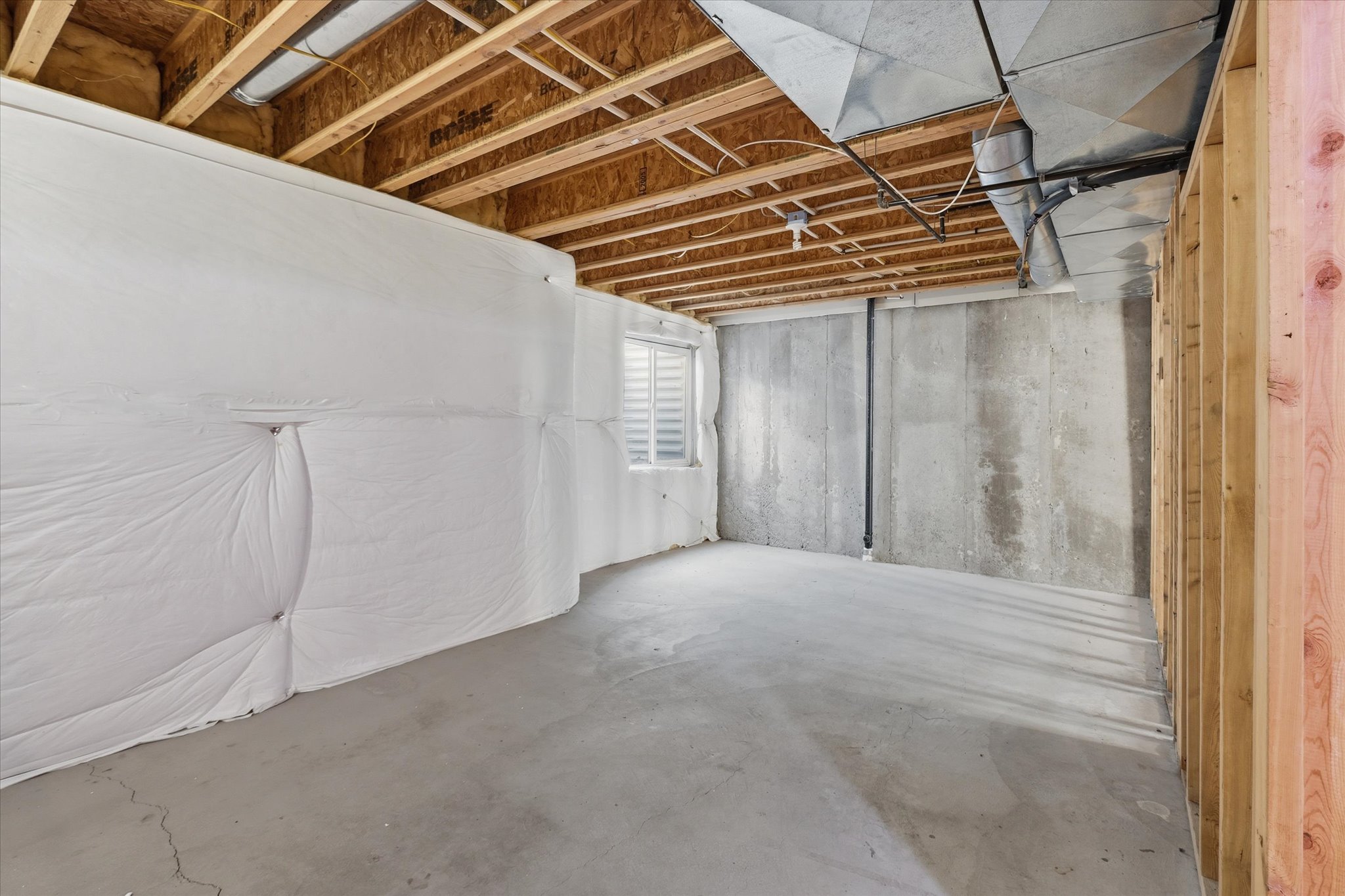 Unfinished basement featuring exposed wood joists, concrete flooring, foundational walls, a single window, and visible HVAC ductwork