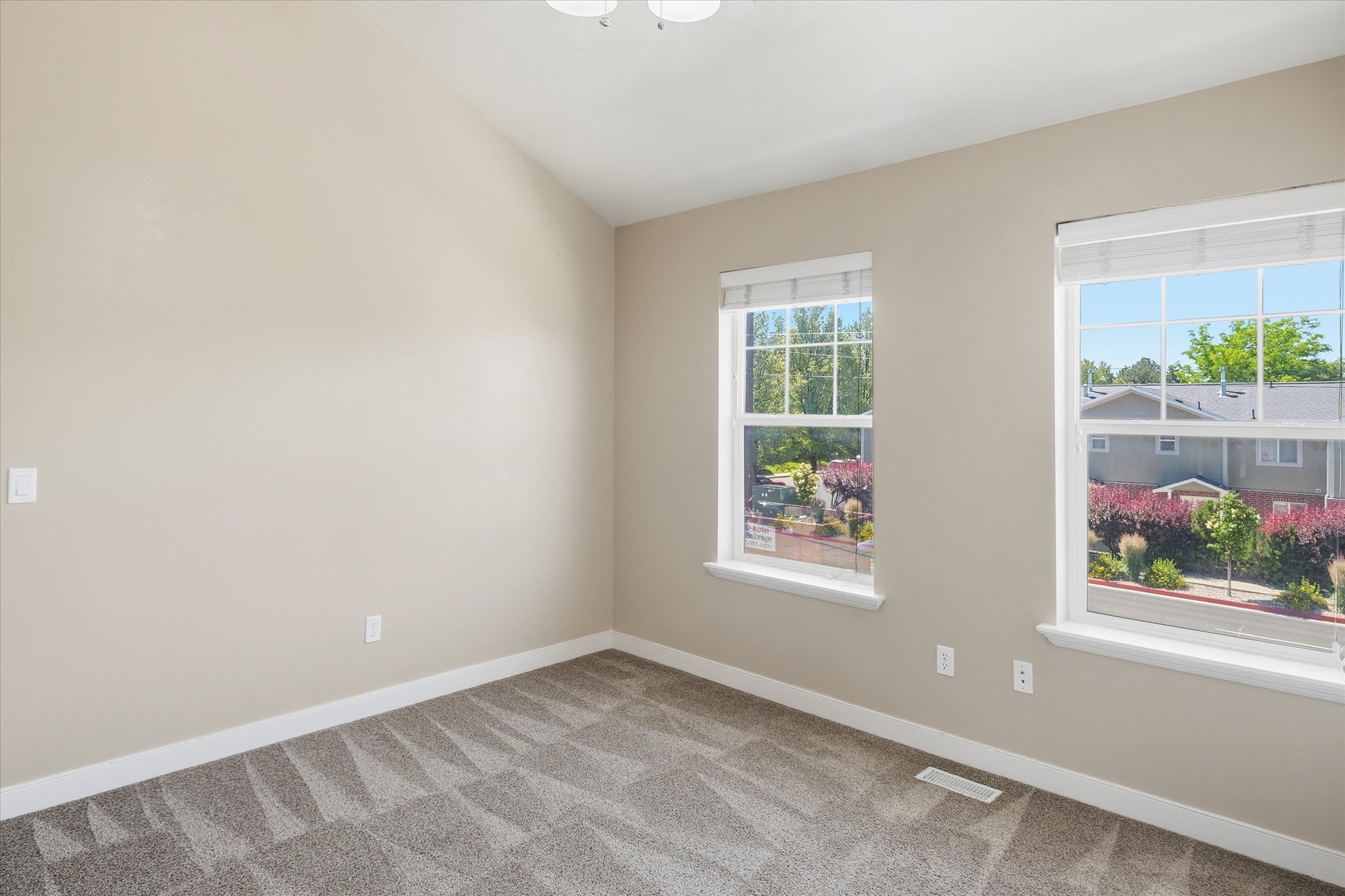 Carpeted room featuring two large windows with blinds, a vaulted ceiling, and neutral-toned walls