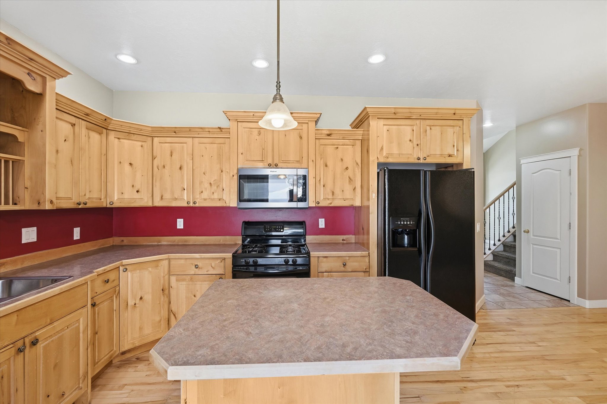 Kitchen featuring wood-finish cabinetry, a central island with a laminate countertop, and a red backsplash