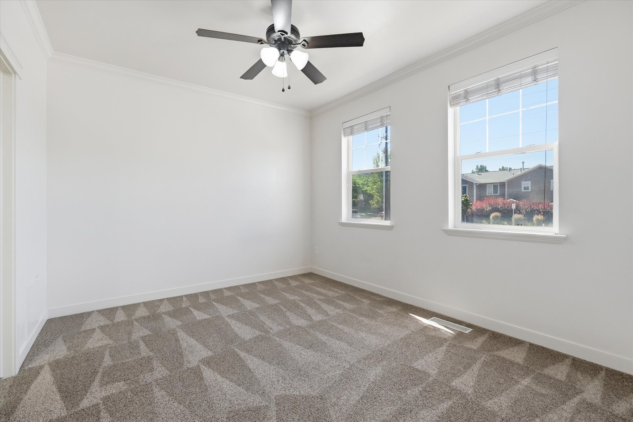 Spacious room featuring patterned carpet, white walls, and a ceiling fan with integrated lighting