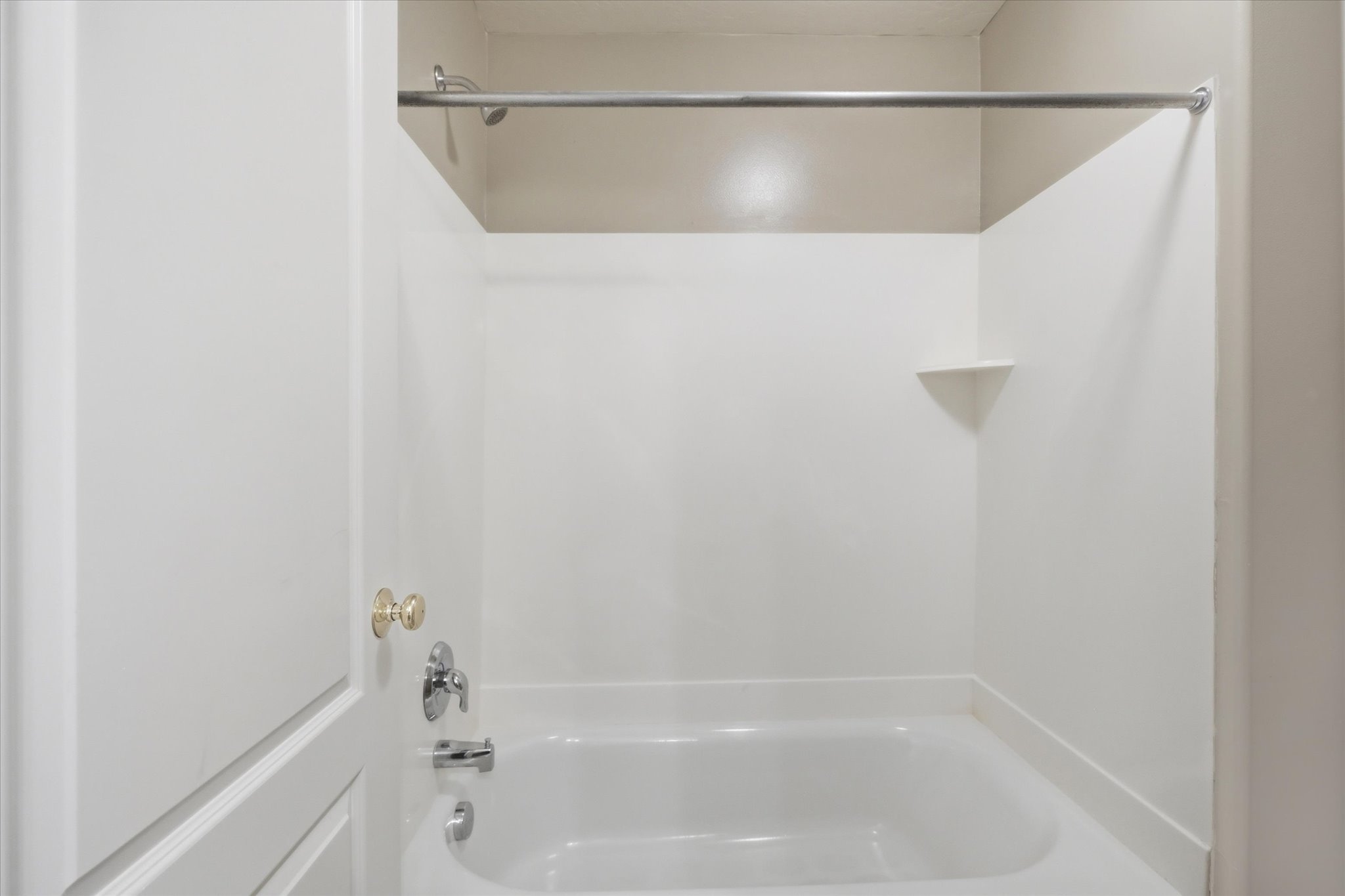 White tub and shower combination featuring a chrome faucet, a corner shelf, and a curved shower rod
