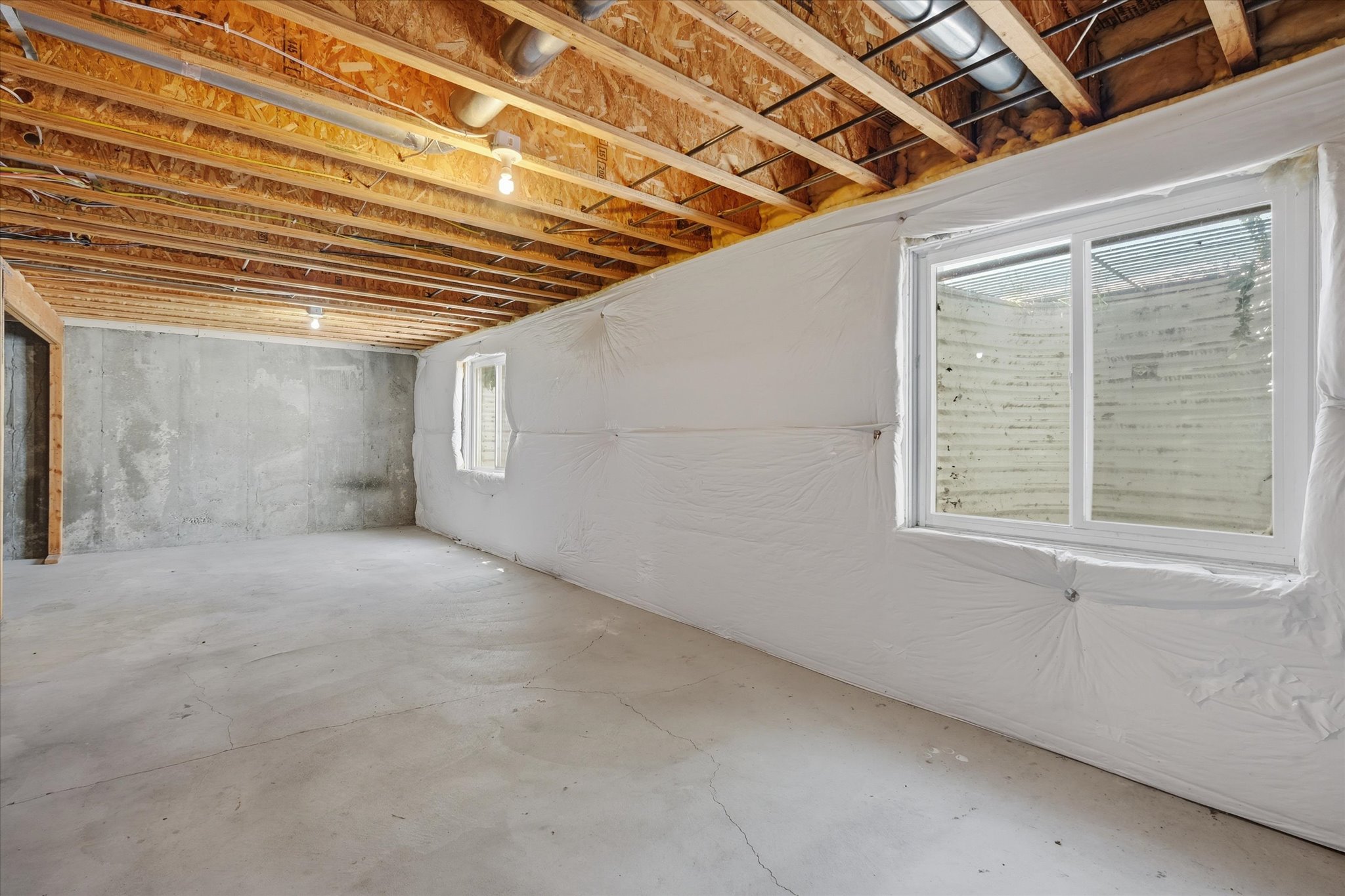 Unfinished basement space featuring exposed wood joists, concrete flooring, and multiple windows