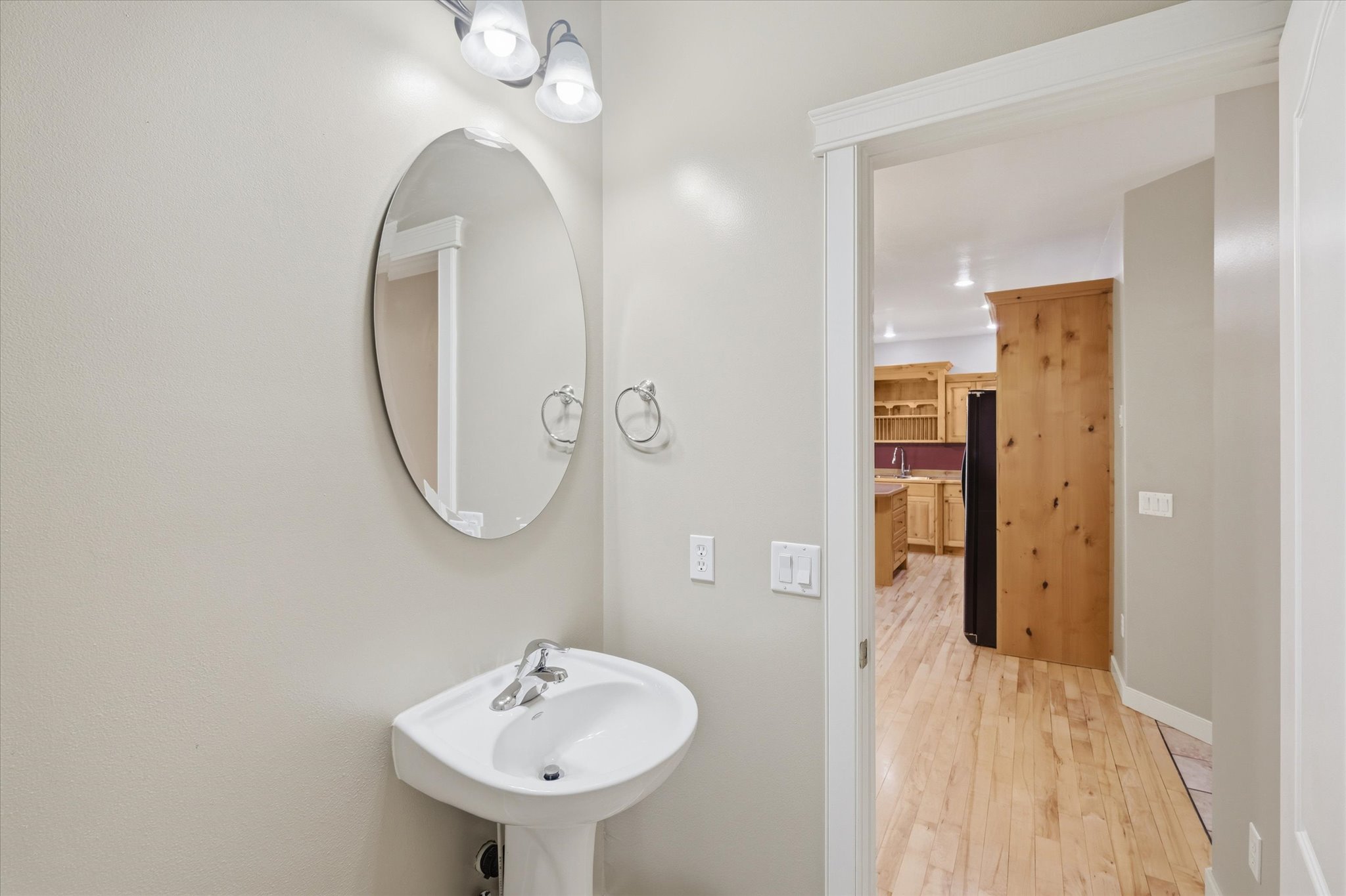 Pedestal sink with chrome faucet, complemented by an oval wall-mounted mirror and overhead vanity lighting
