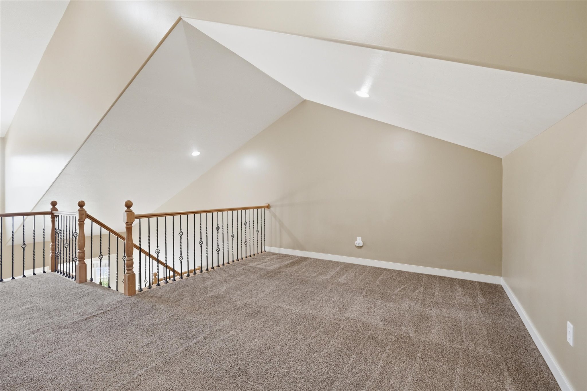 Carpeted loft area featuring a wood handrail with wrought iron balusters, angled ceilings, and recessed lighting