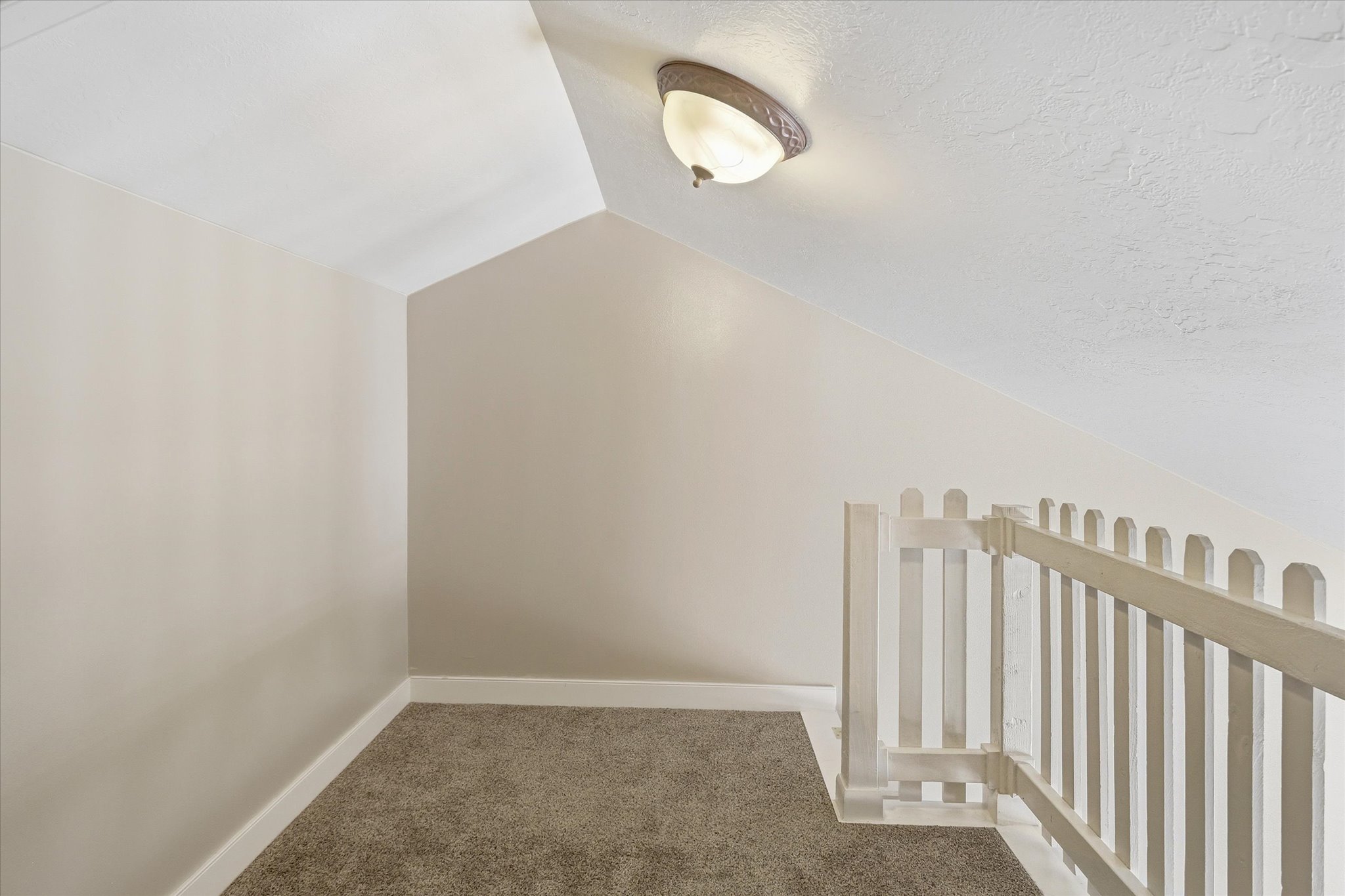 Carpeted loft area featuring sloped ceilings, a semi-flush mount ceiling light, and a white picket-style railing