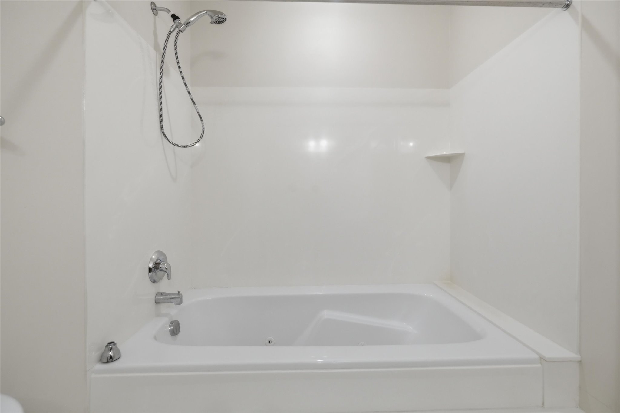 White bathtub with integrated shower, chrome fixtures, and a corner shelf