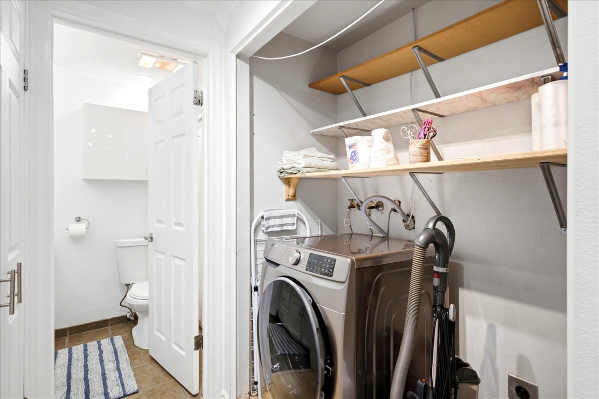 Dedicated laundry area featuring a front-load washer, wall-mounted shelving, and plumbing hookups