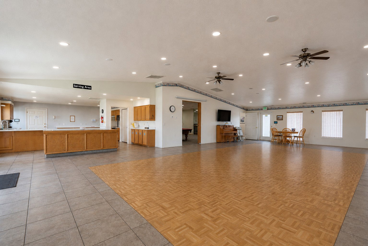Expansive interior space featuring a light wood-finish dance floor, tile flooring, and a serving area with wood cabinetry