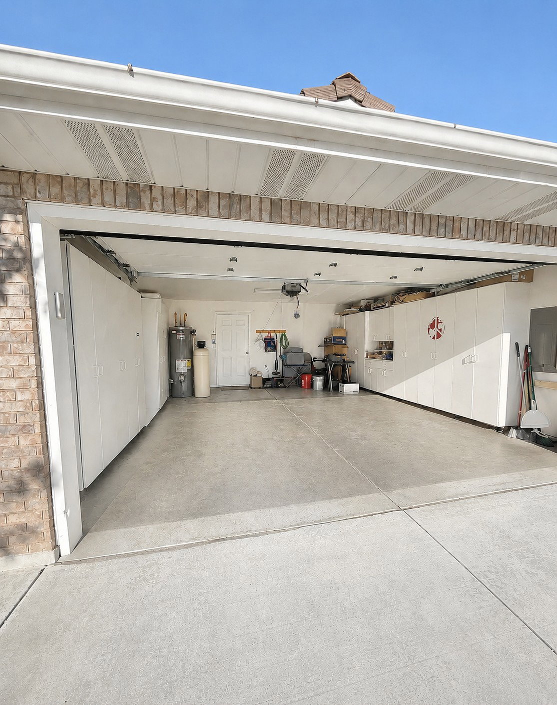 Spacious garage featuring a durable epoxy floor coating, extensive built-in cabinetry, and a brick exterior facade