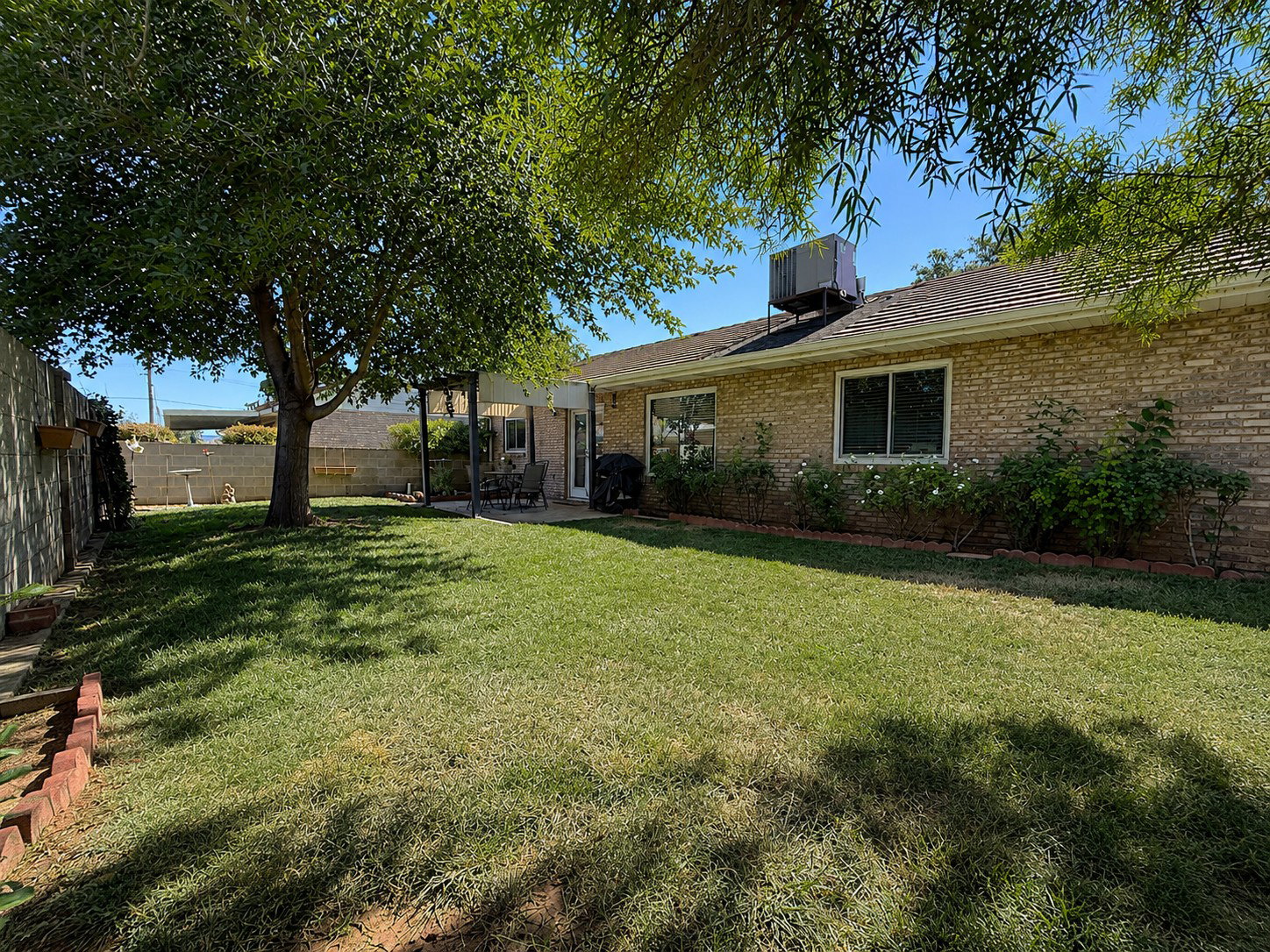 Expansive backyard featuring a mature shade tree, a brick perimeter wall, and a covered patio area