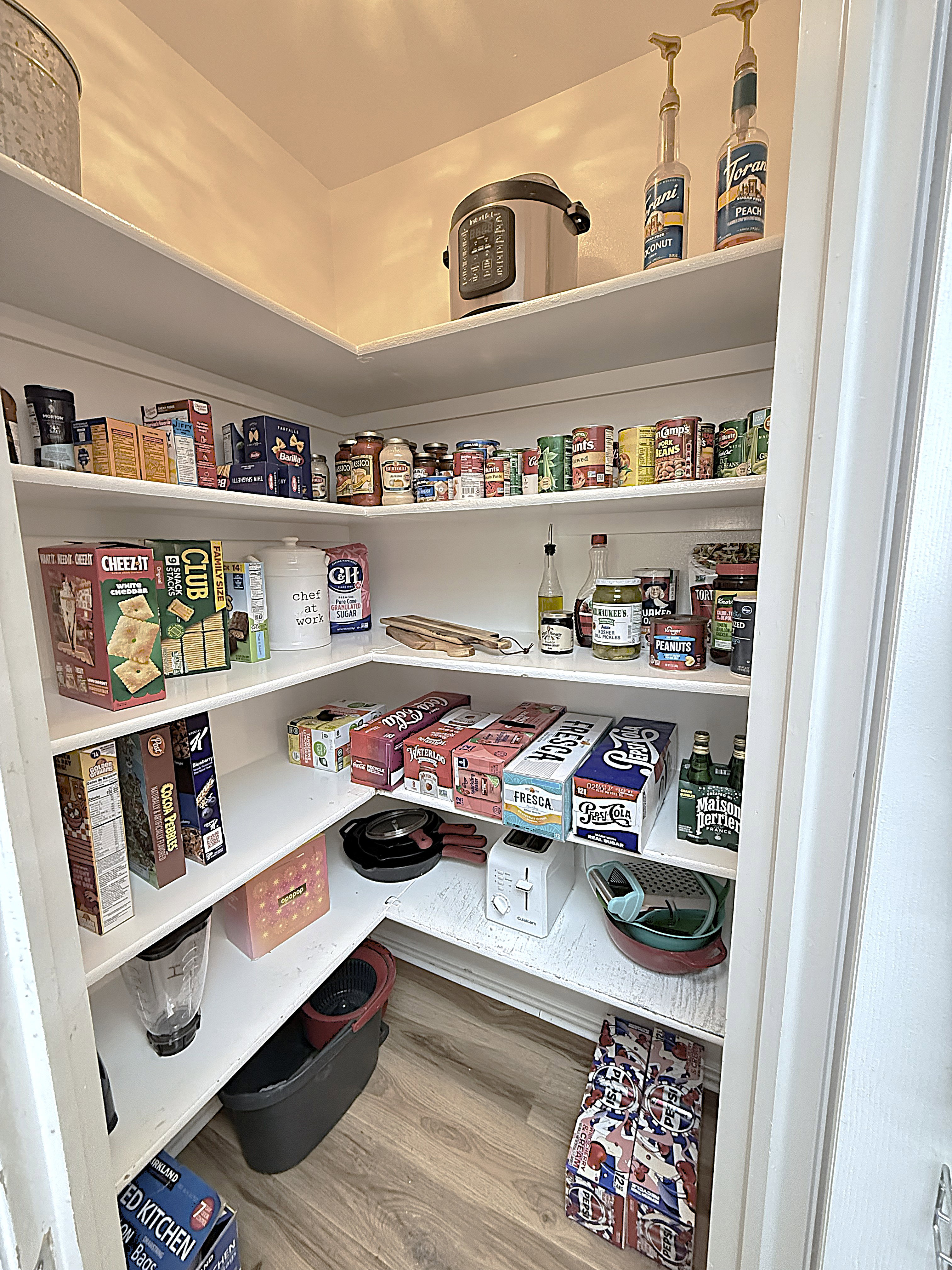 Corner pantry with multiple levels of shelving and wood-finish flooring