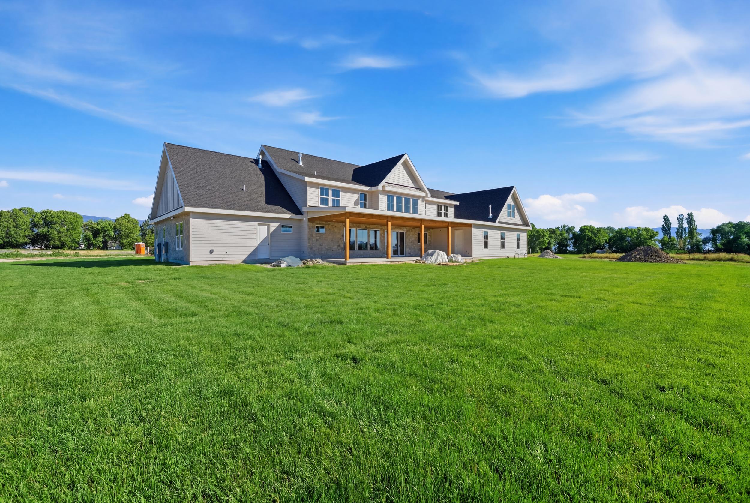 Expansive green lawn surrounds a newly constructed residence featuring light-colored siding, a dark shingle roof, and a covered back patio with natural wood posts