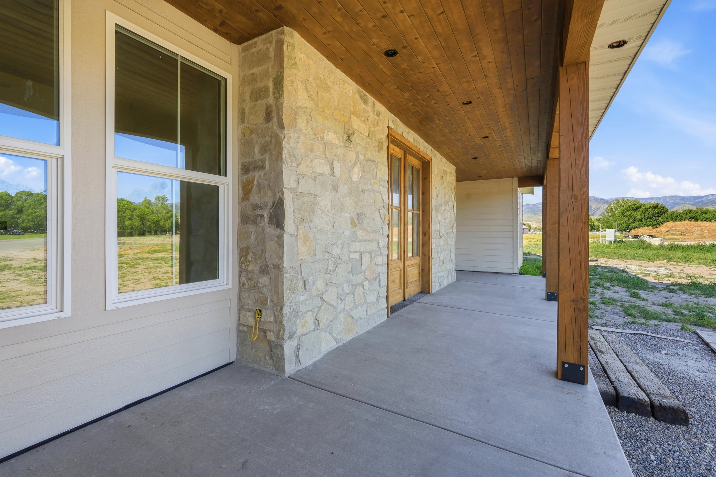 Expansive covered porch featuring a natural wood-finish ceiling, exposed structural beams, and stone veneer accents