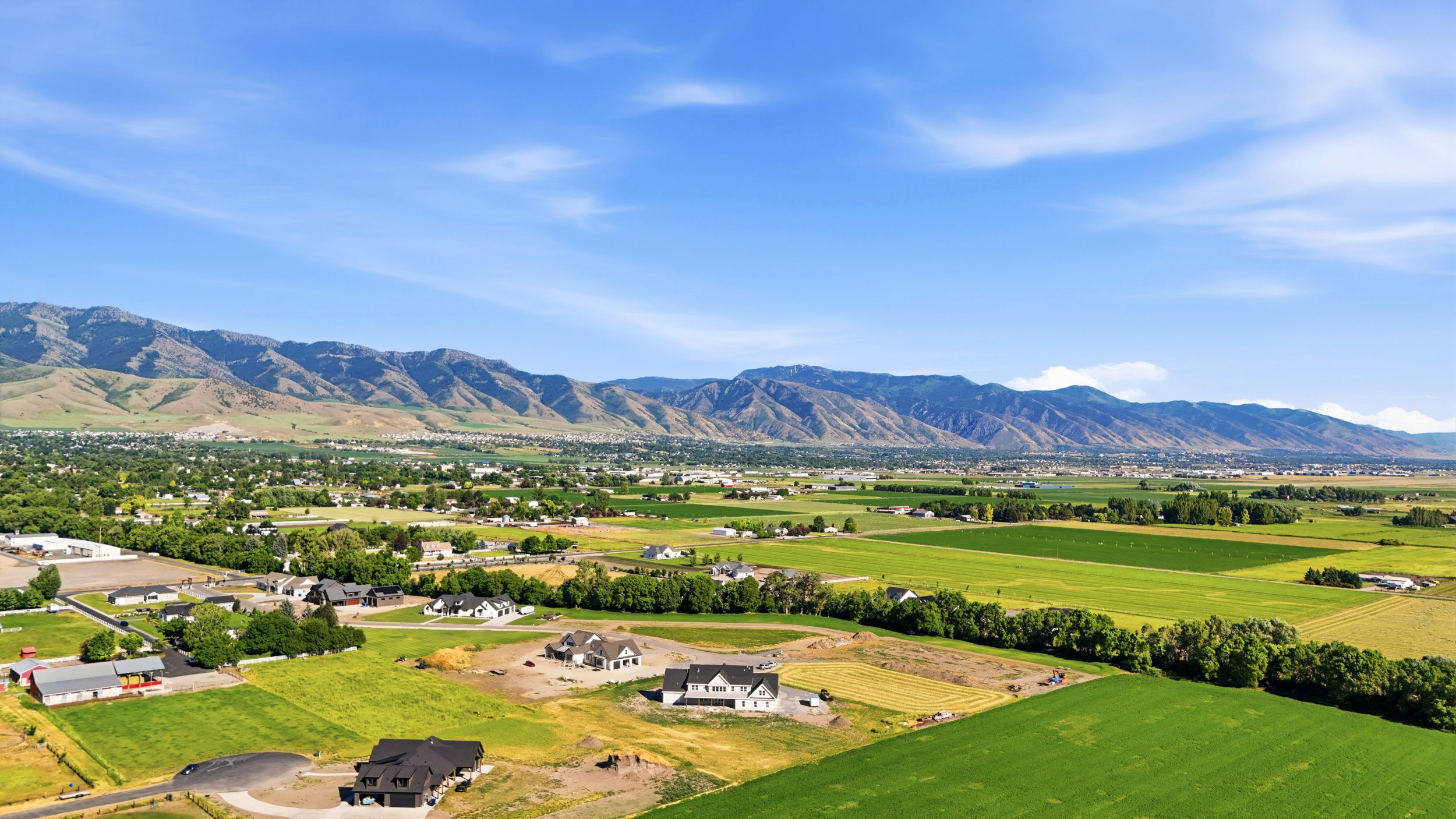 Expansive landscape featuring distant mountains, verdant fields, and scattered residential properties